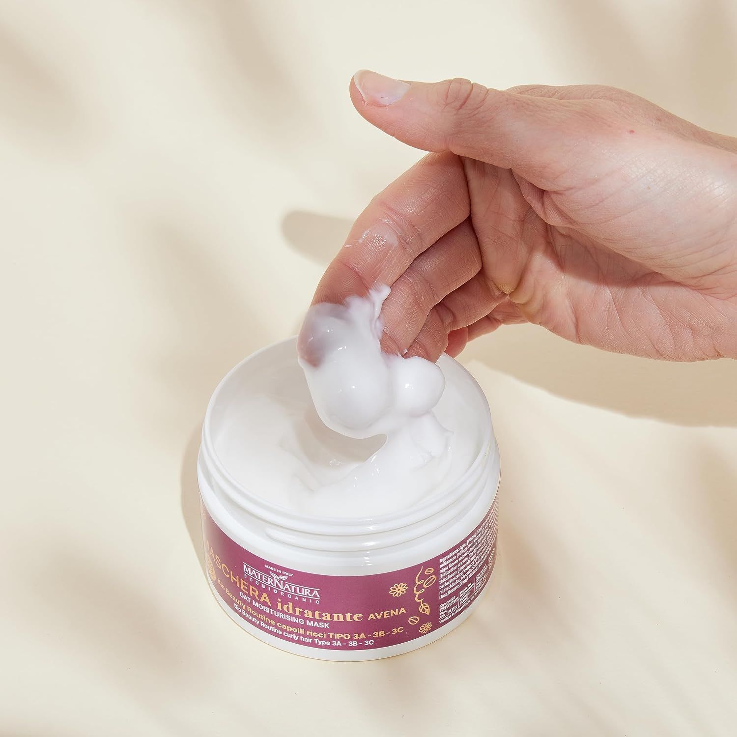 Eine Hand entnimmt eine weiße Creme aus einem weißen Tiegel mit lila Etikett.