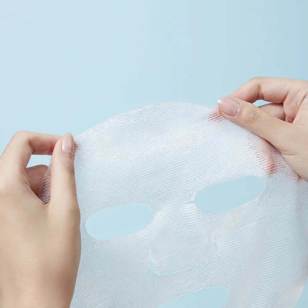 Gesichtsmaske aus weißem Stoff, gehalten von zwei Händen. Aussparungen für Augen, Nase und Mund sichtbar.