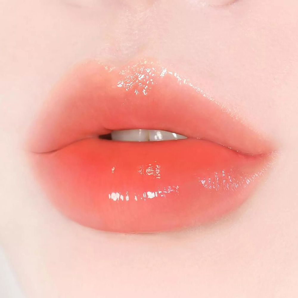 Nahaufnahme von Lippen, die mit einem glänzenden, orangefarbenen Lippenbalsam bedeckt sind. Die Lippen sind leicht geöffnet.