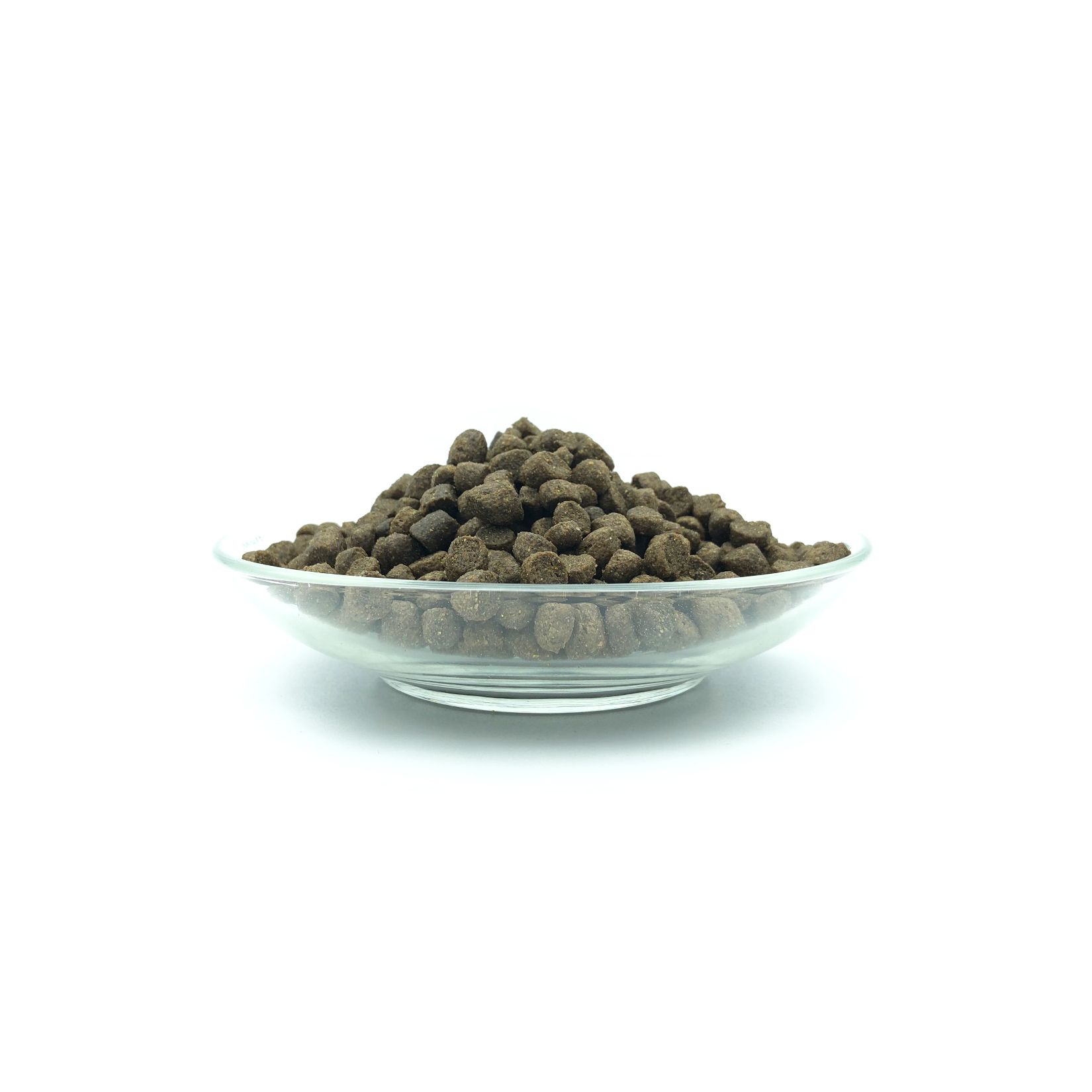 Haufen brauner, runder Trockenfutter-Pellets in einer transparenten Glasschale. Auf weißem Hintergrund.