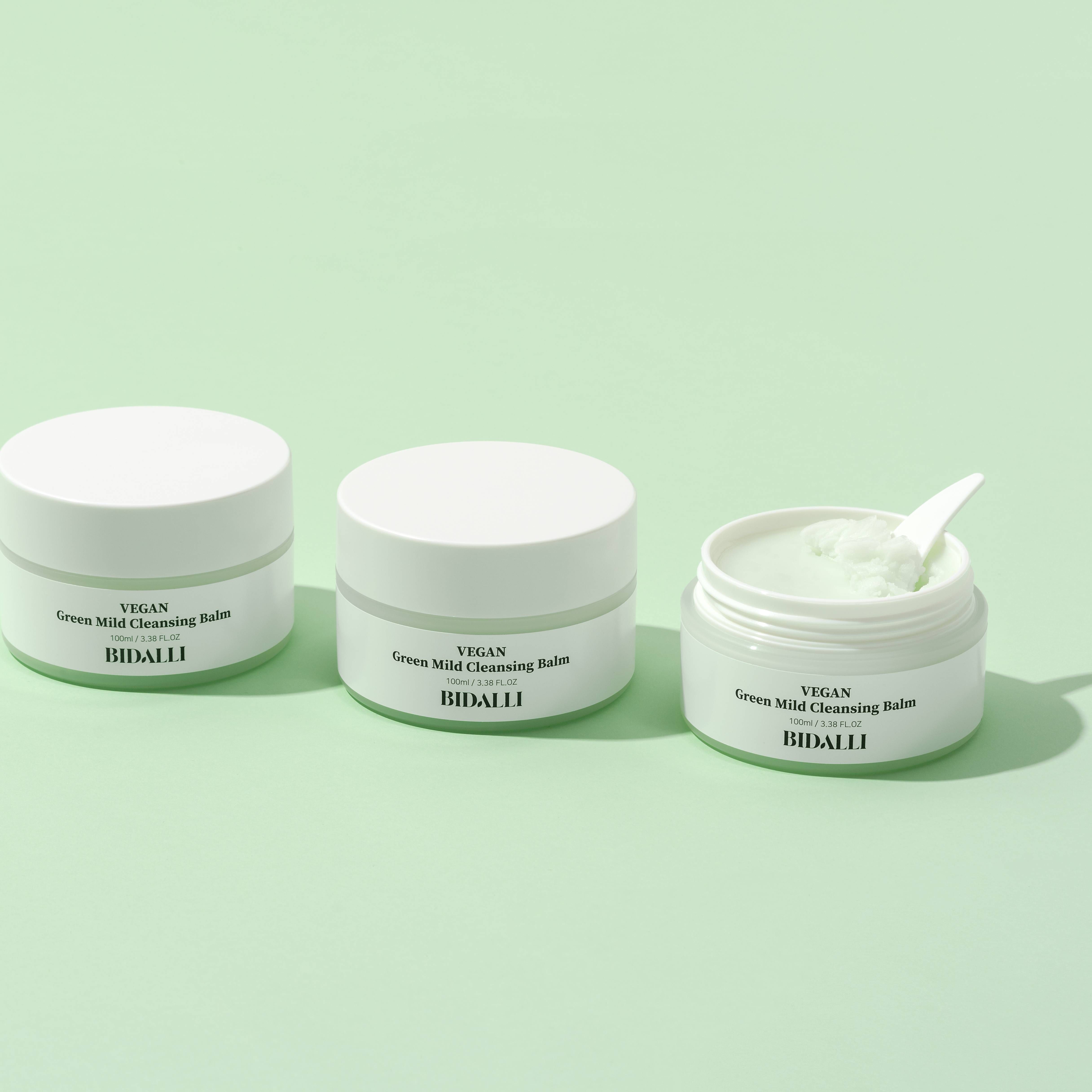 Drei Tiegel mit Deckel. Einer ist geöffnet mit grünem Balsam und Spatel. Auf den Etiketten steht: VEGAN Green Mild Cleansing Balm. BIDALLI.