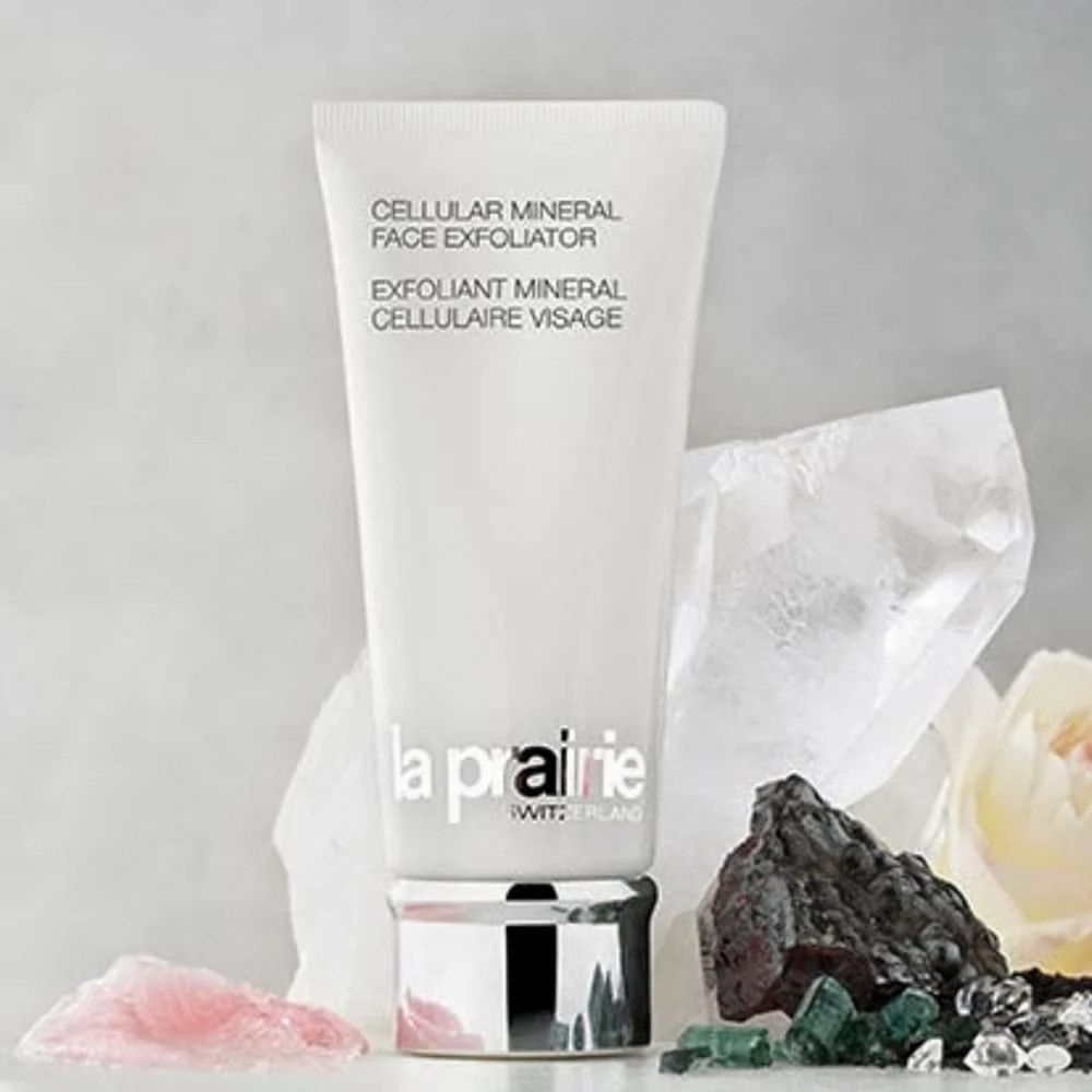 Weiße Tube mit Produkttext und Logo. Umgeben von Steinen und Blüten. Marke: La Prairie.