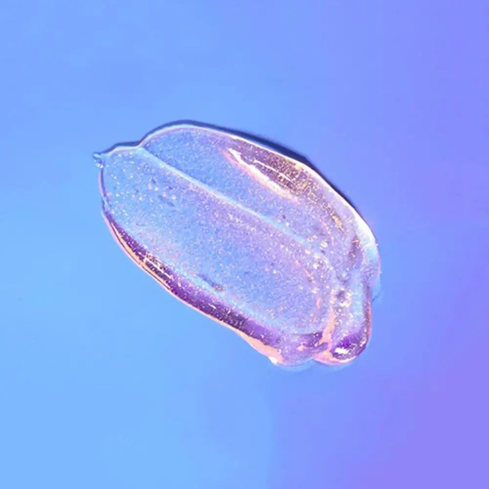 Transparente Gelprobe mit Glitzerpartikeln auf blau-violettem Hintergrund.