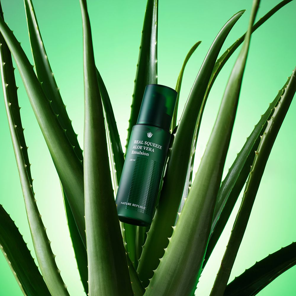 Grüne Flasche mit Aufschrift: REAL SQUEEZE ALOE VERA Emulsion, umgeben von Aloe Vera Blättern.