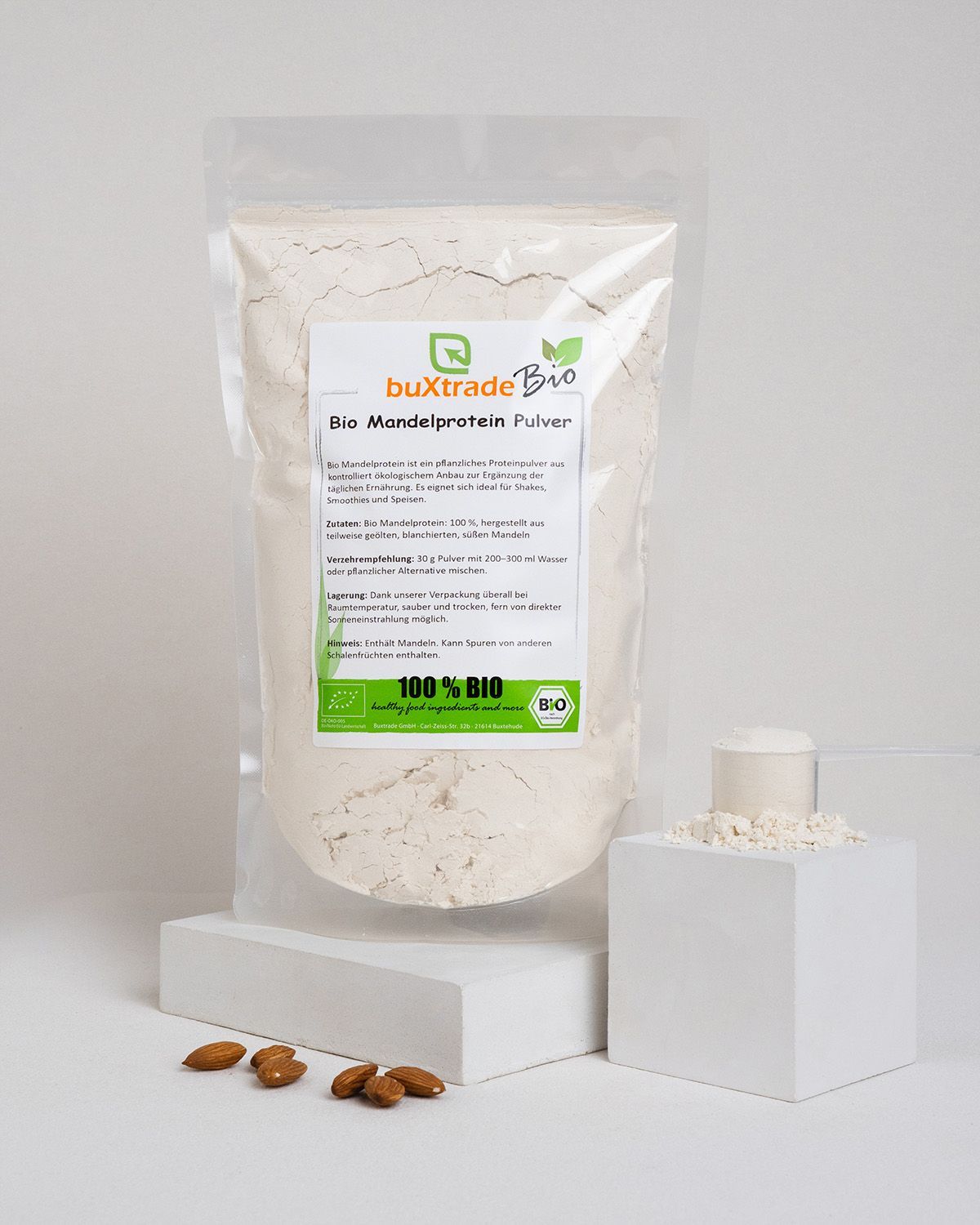 Ein Beutel buxtrade Bio Mandelprotein Pulver, daneben ein Löffel mit Pulver und Mandeln.