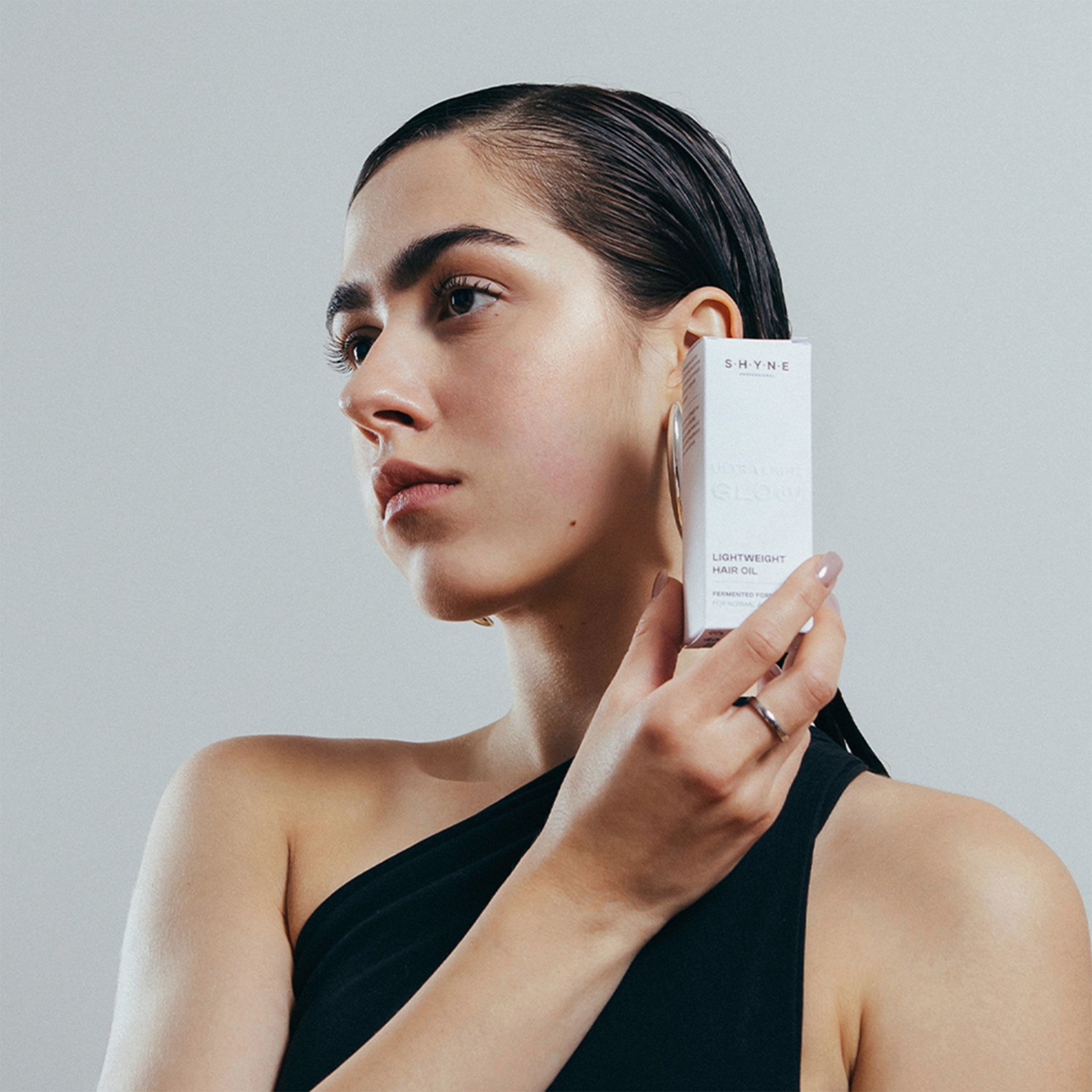 Frau hält eine Schachtel mit der Aufschrift SHYNE. Auf der Schachtel steht: LIGHTWEIGHT HAIR OIL.