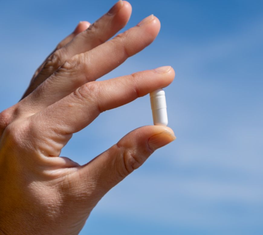 Hand hält eine einzelne Magnesiumcitrat-Kapsel vor blauem Himmel.