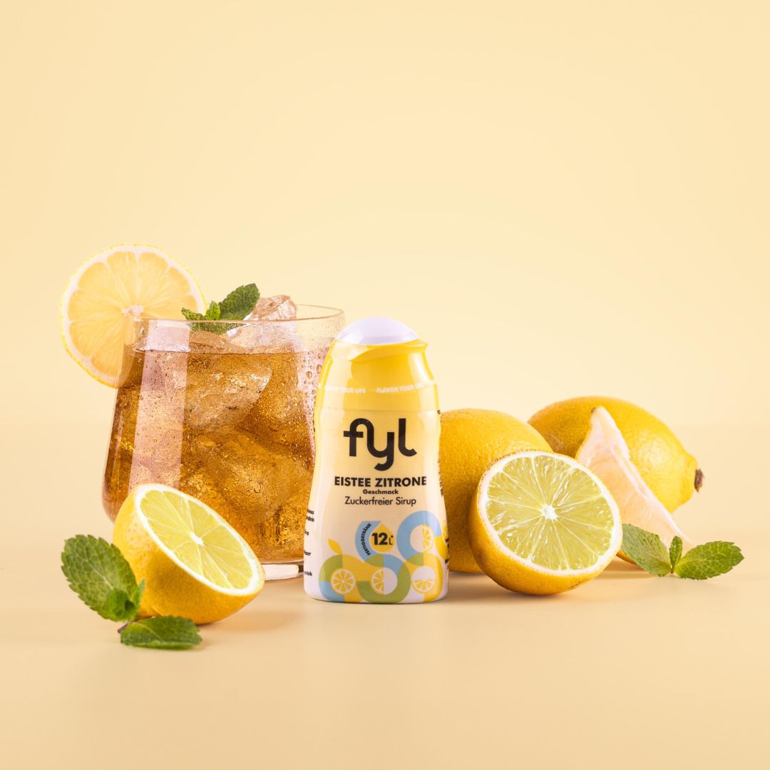 Flasche fyl Eistee Zitrone Sirup, neben Zitronen, Minze und einem Glas Eistee. Aufschrift: 12 Portionen.