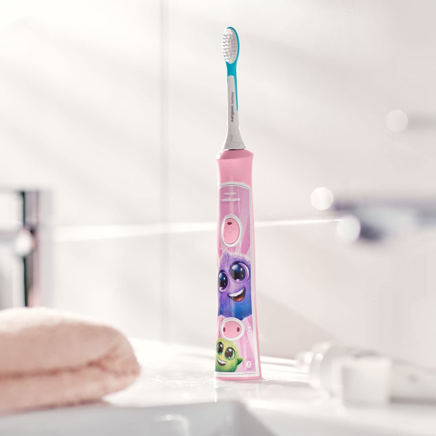 Pinke elektrische Zahnbürste für Kinder. Aufdrucke: Philips Sonicare. Bürstenkopf. Waschbecken und Handtuch im Hintergrund.