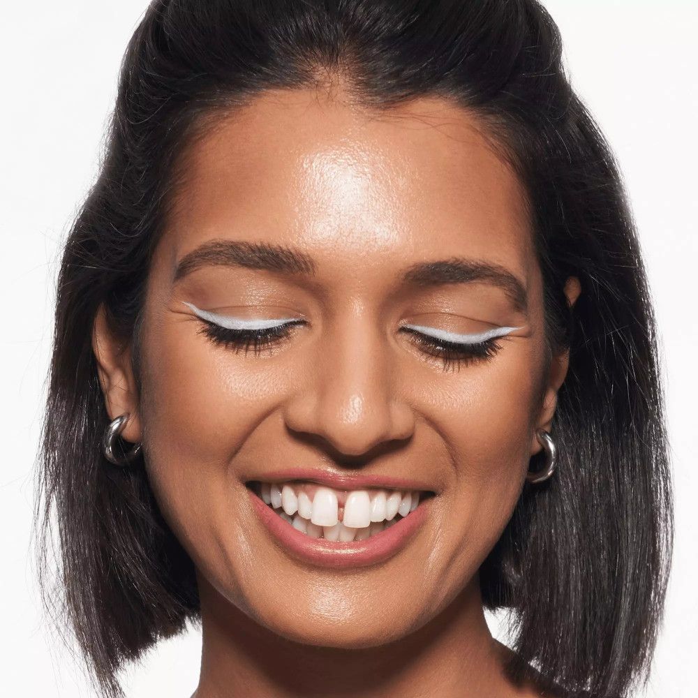 Frau mit weißem Eyeliner auf den Augenlidern. Sie lächelt.