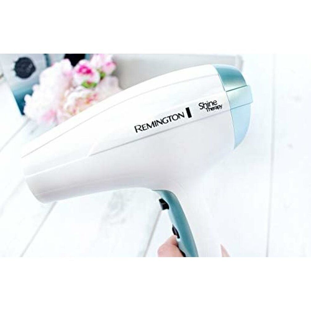 Weißer Haartrockner. Marke Remington Shine Therapy. Blaue Akzente. In der Hand gehalten.