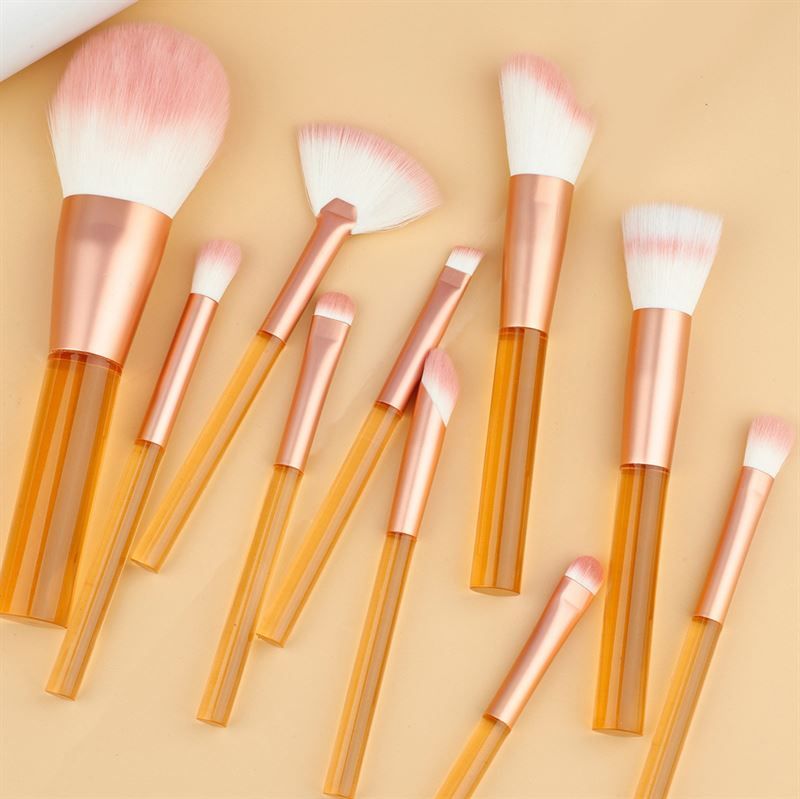 Set aus Make-up-Pinseln mit transparenten, orangefarbenen Griffen und rosa Borsten. Verschiedene Formen und Größen.