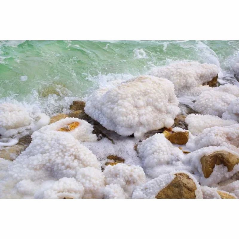 Nahaufnahme von Felsen am Ufer, bedeckt mit weißem Salz. Wellen schlagen gegen die Felsen.