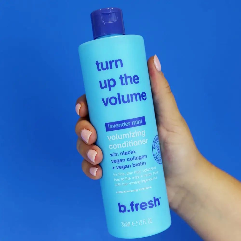 Hellblaues Shampoo mit blauem Deckel. Aufschrift: Turn up the volume, volumizing conditioner. Marke: b.fresh. Hand hält die Flasche.