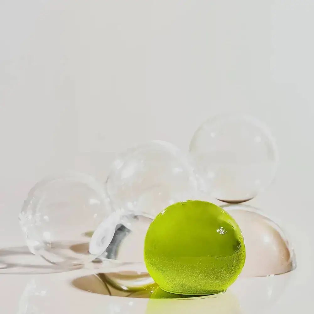 Grünliche Kugel auf transparenten Halbkugeln. Mehrere transparente Kugeln. Helles Ambiente.