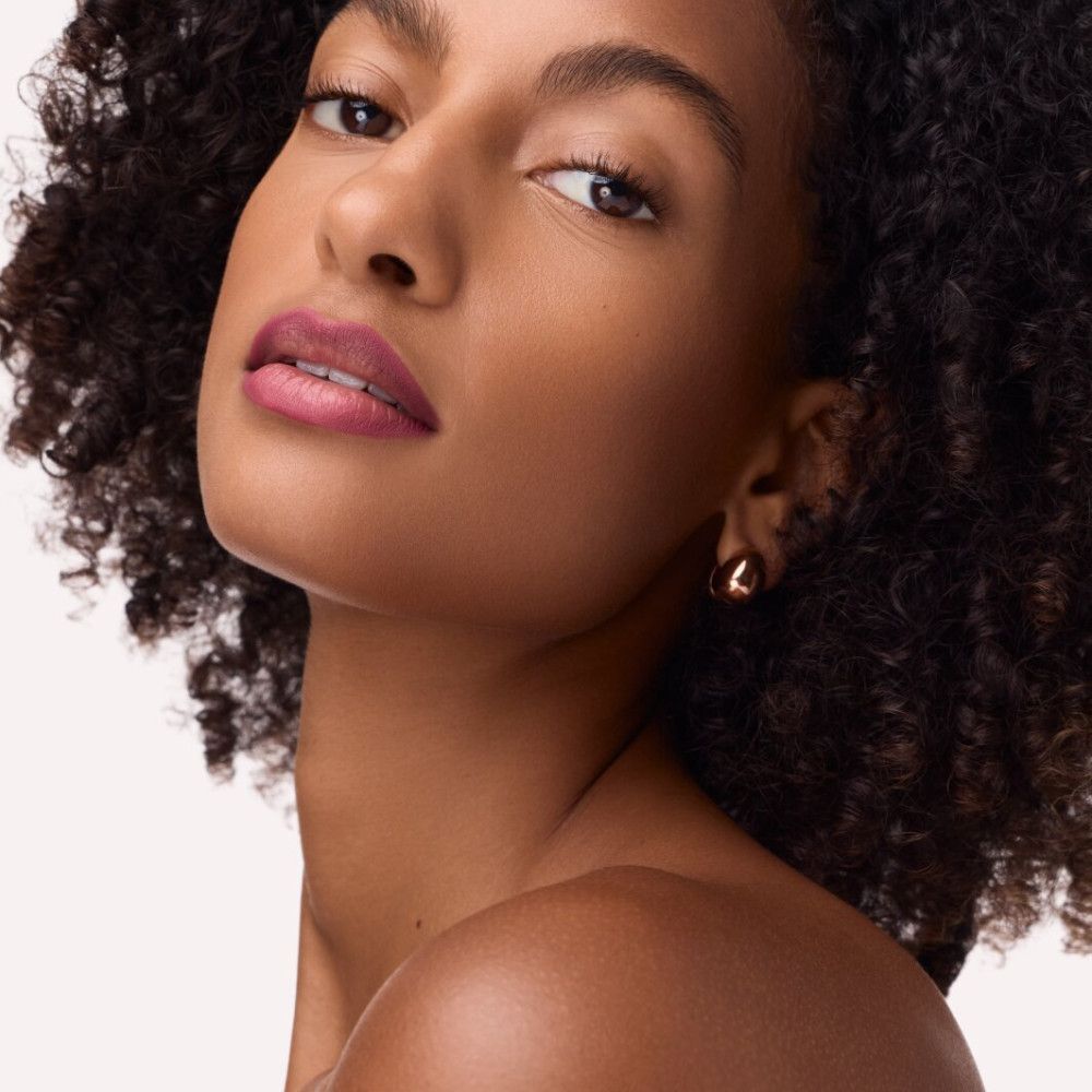 Porträt einer Frau mit Locken und Lippenstift. Sie trägt goldene Ohrringe.