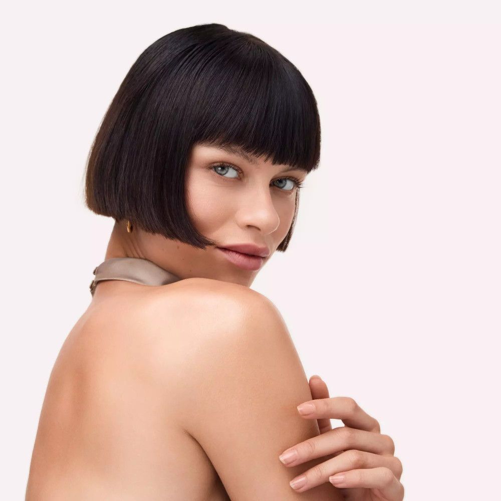 Porträt einer Frau mit Bob-Frisur. Sie trägt ein beiges Oberteil und schaut zur Seite.