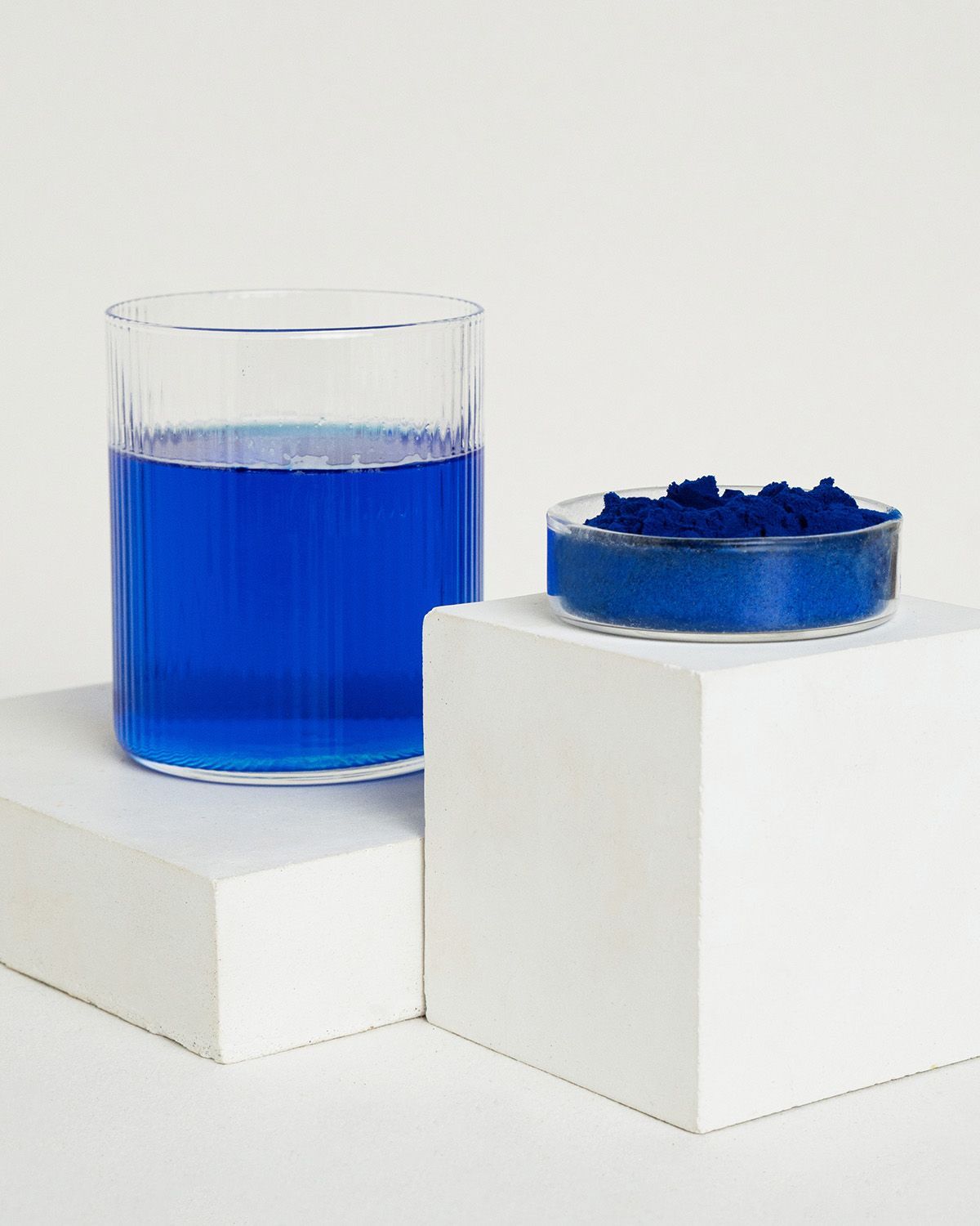 Ein Glas mit blauem Getränk und eine Schale mit blauem Pulver auf weißen Würfeln.