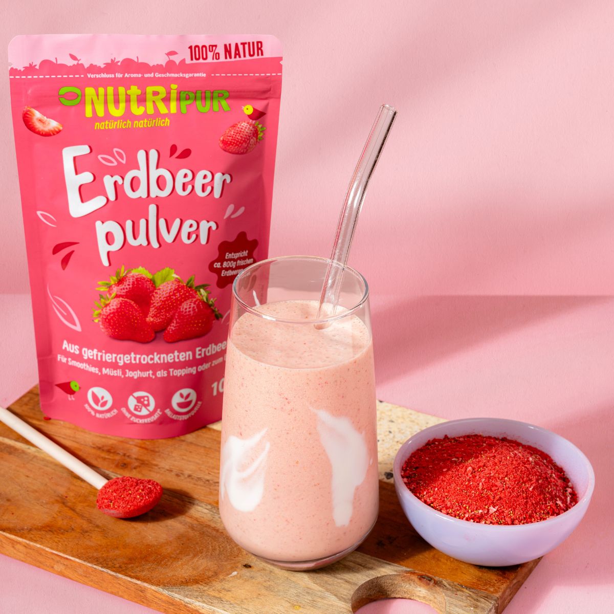 Rosa Beutel mit Erdbeerpulver, Glas mit Erdbeergetränk, Schale mit Pulver, Löffel. Marke: NutriPur.
