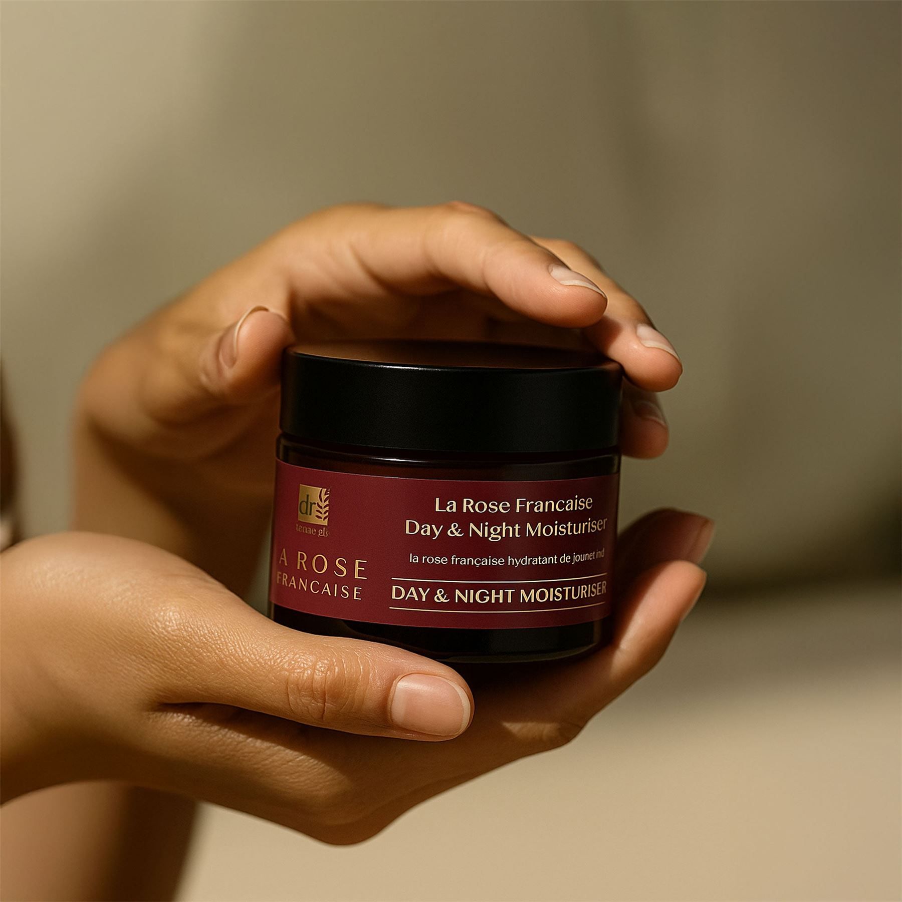 Hände halten ein Glas Dr. Botanicals La Rose Française Tages- und Nachtcreme.