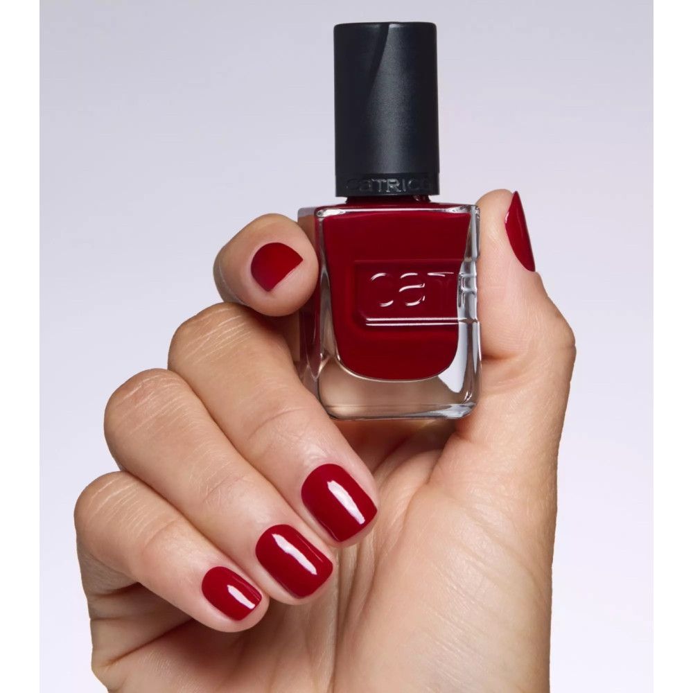 Hand mit lackierten Nägeln. Roter Nagellack. Nagellackflasche mit schwarzem Deckel. "catrice" Schriftzug.