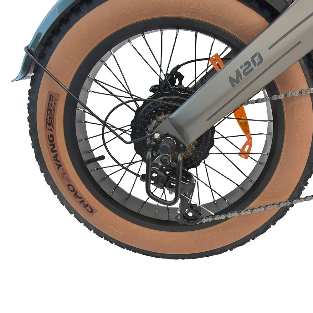 Nahaufnahme des Hinterrads einer grauen Elektrodirtbike. Brauner Reifen, schwarze Kette und Details. Aufschrift 'M20'.