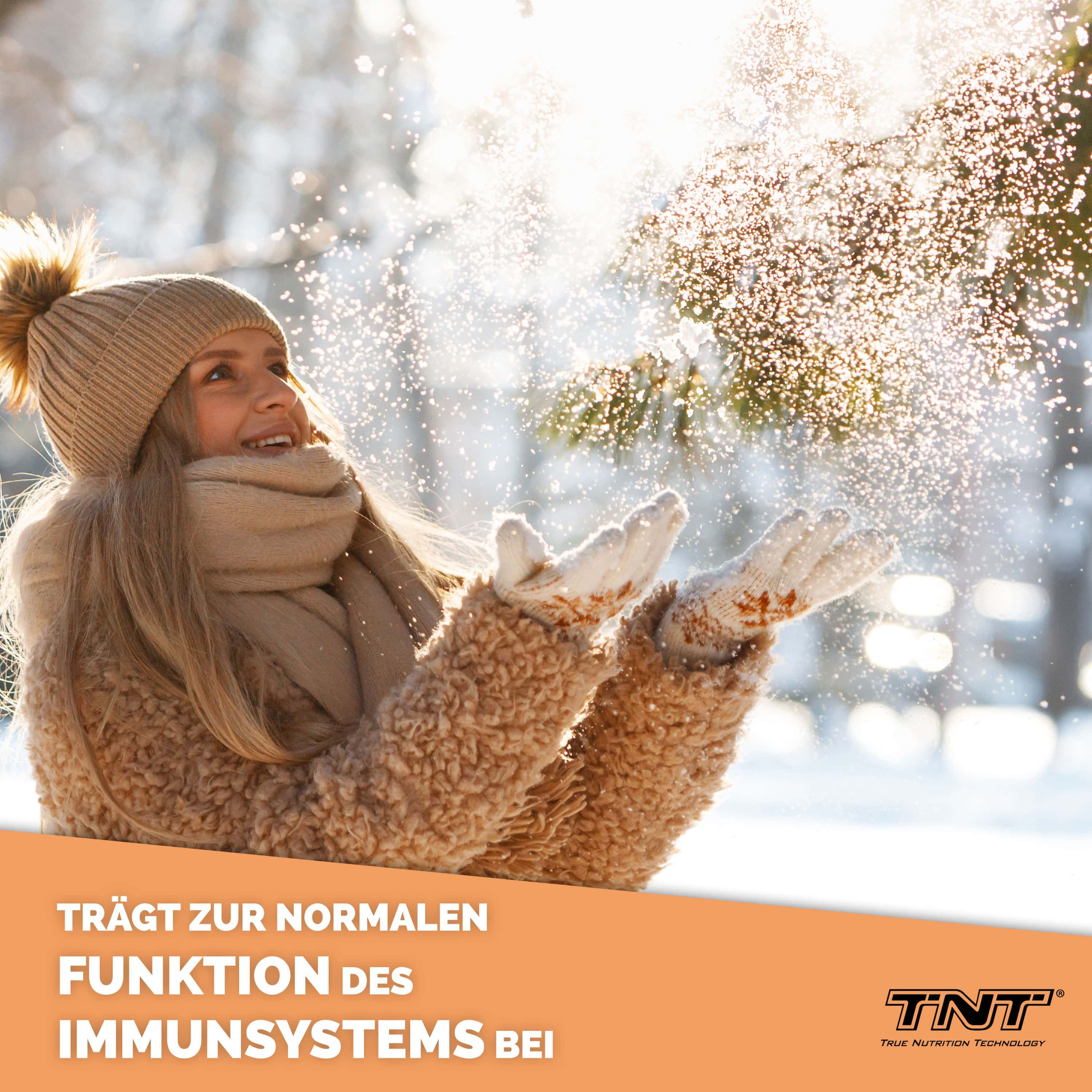 Frau im Winter wirft Schnee in die Luft. Text: Trägt zur normalen Funktion des Immunsystems bei. TNT Logo.
