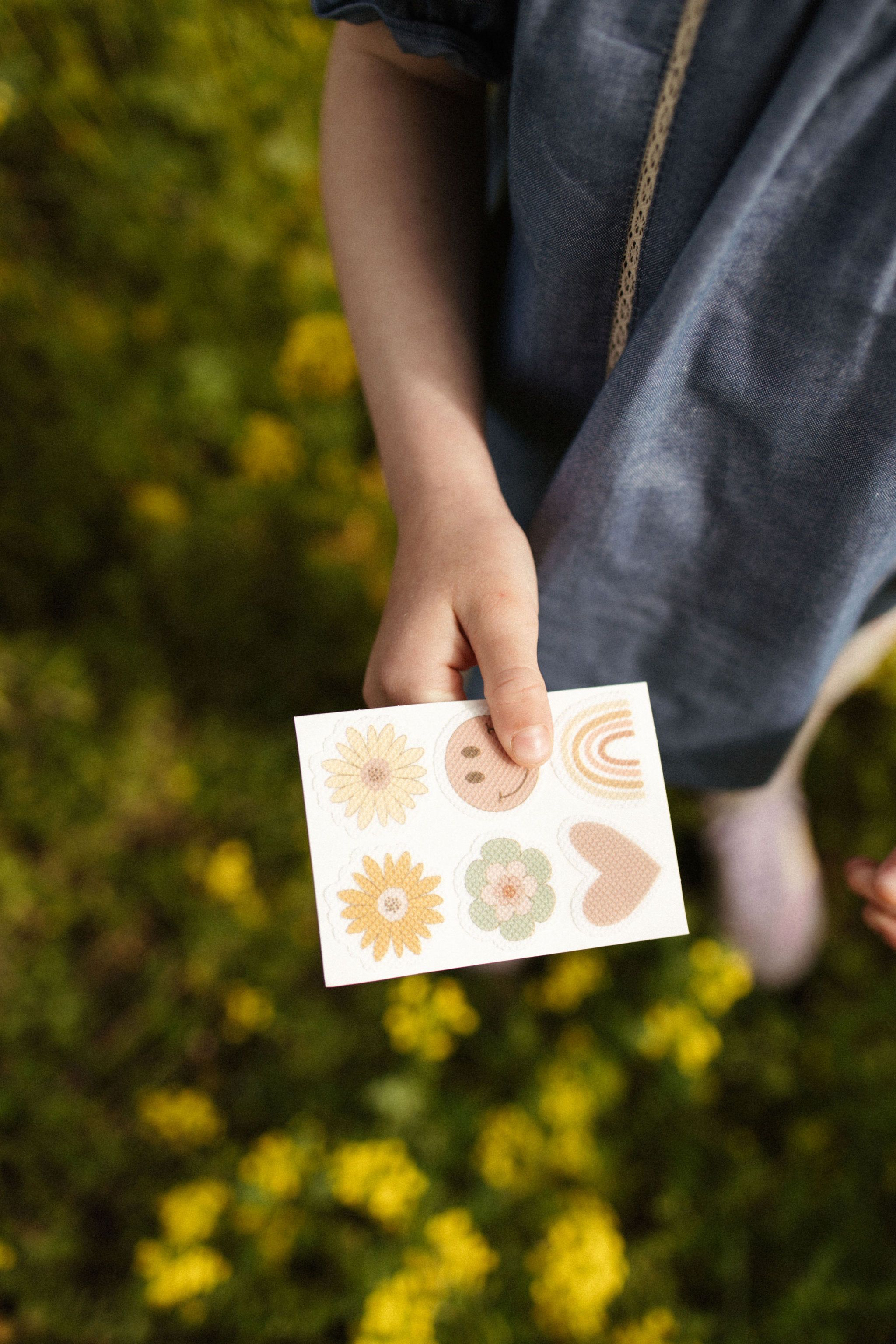 Kind hält Sticker mit Blumen-, Herz- und Smiley-Motiven. Auf weißem Hintergrund.