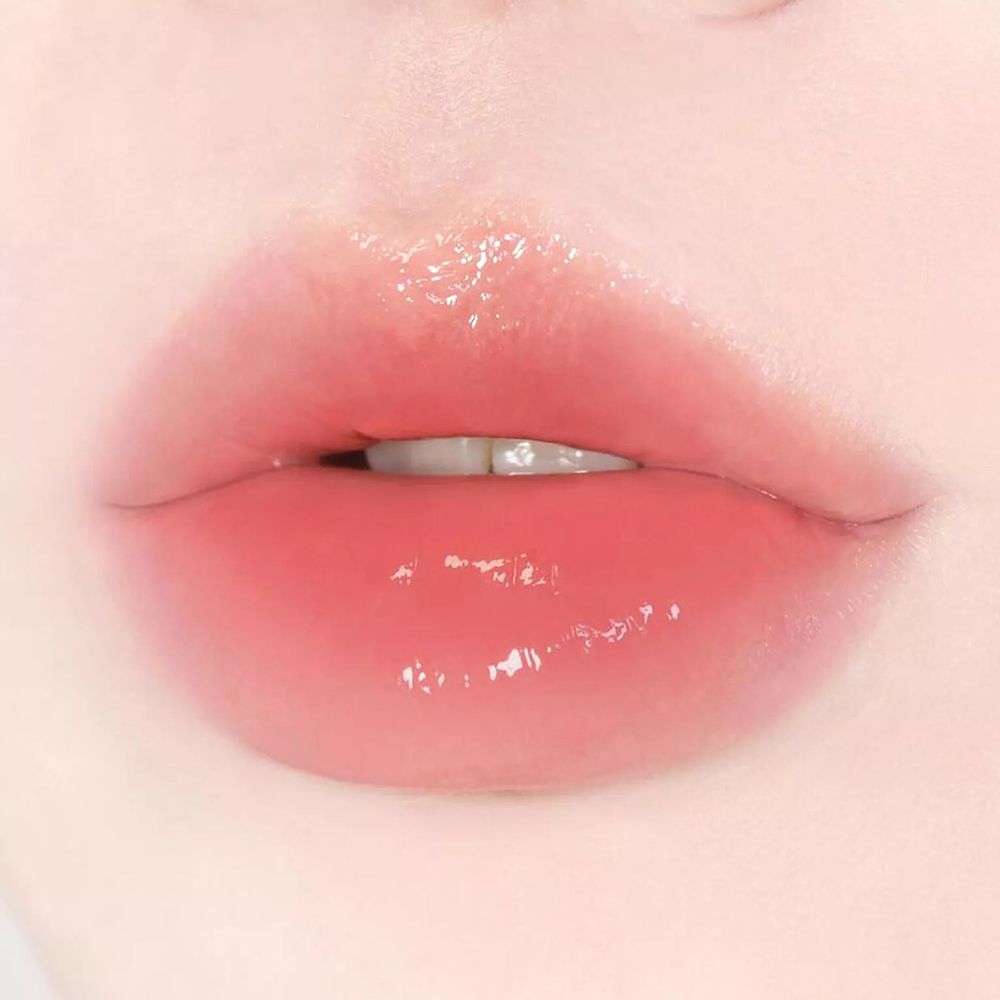Nahaufnahme von Lippen mit glänzendem, rosa Lippenbalsam. Zähne sichtbar.