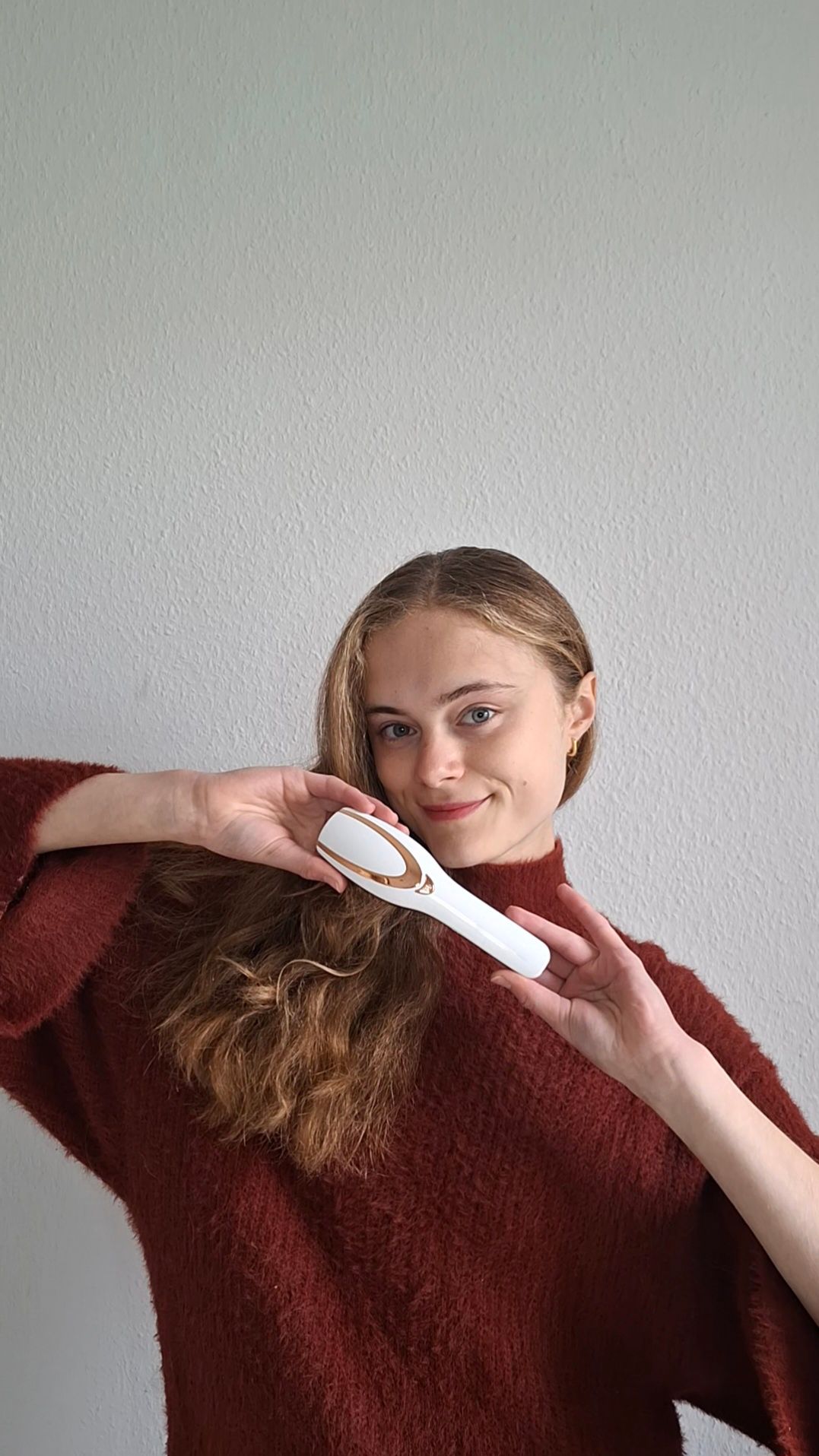 Weiß-goldener Haarbürsten-Apparat. Frau hält das Gerät vor ihren Haaren. Gerät hat eine ovale Form.