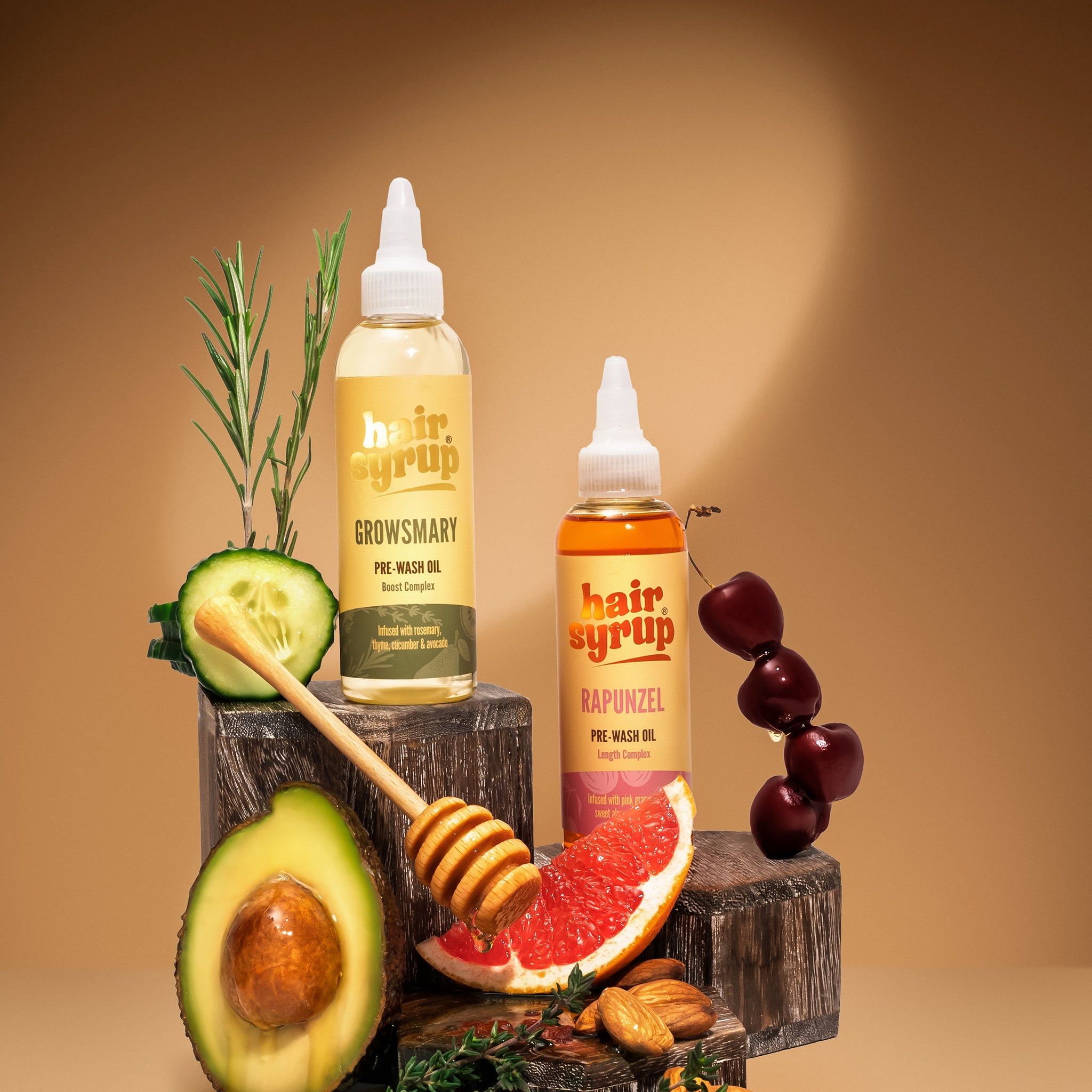 Zwei Flaschen Hair Syrup, eine mit der Aufschrift 'Growsmary', die andere 'Rapunzel'. Dazu Avocado, Honig und Grapefruit.