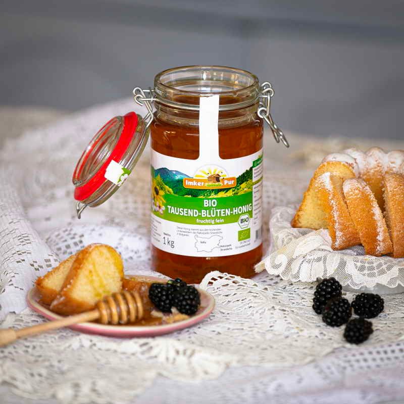 Honigglas mit Etikett neben Kuchen und Beeren. Honig auf Teller mit Honiglöffel.