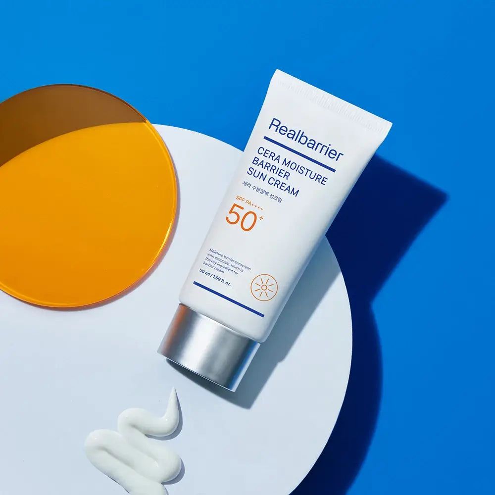 Weiße Tube mit Sonnencreme, daneben eine orangefarbene Scheibe. Aufschrift: Realbarrier Cera Moisture Barrier Sun Cream SPF 50+.