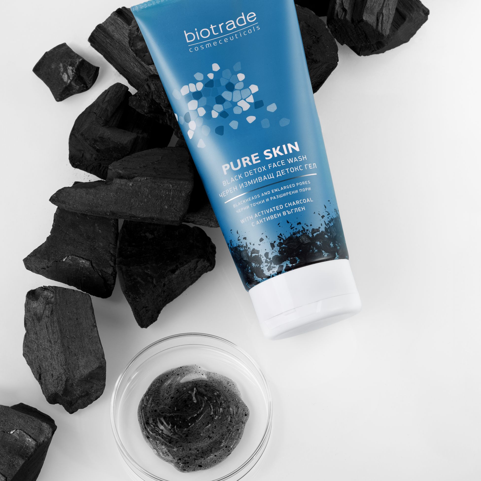 Blaue Tube mit Produktnamen und Text, neben Holzkohle und einer Glasschale mit schwarzem Gel. Aufschrift: Pure Skin Black Detox.