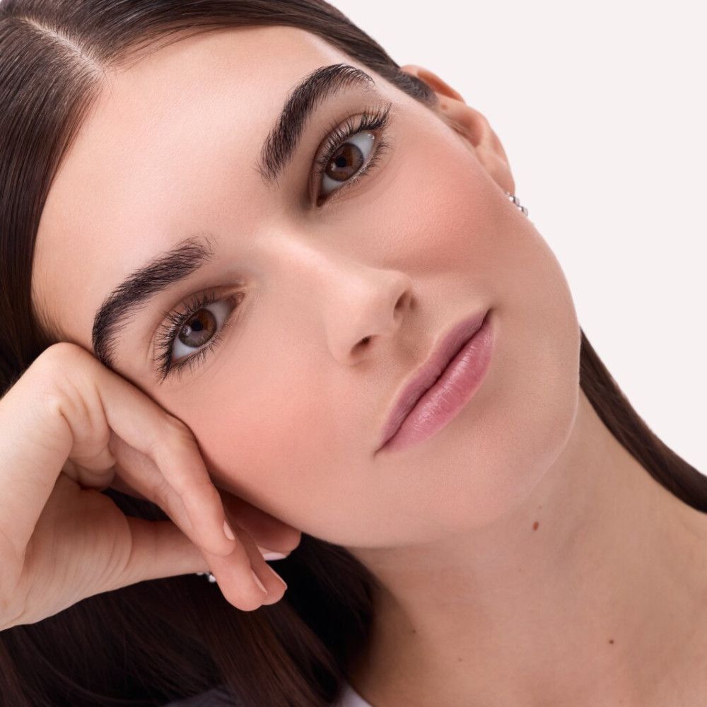 Porträt einer Frau mit Rouge auf den Wangen. Sie stützt ihr Kinn mit der Hand.