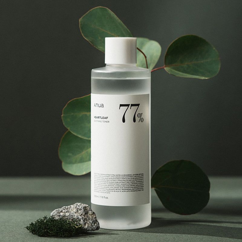 Transparente Flasche mit weißem Deckel, umgeben von Blättern und einem Stein. Aufkleber mit Text: Anua, Heartleaf 77%, 77%.