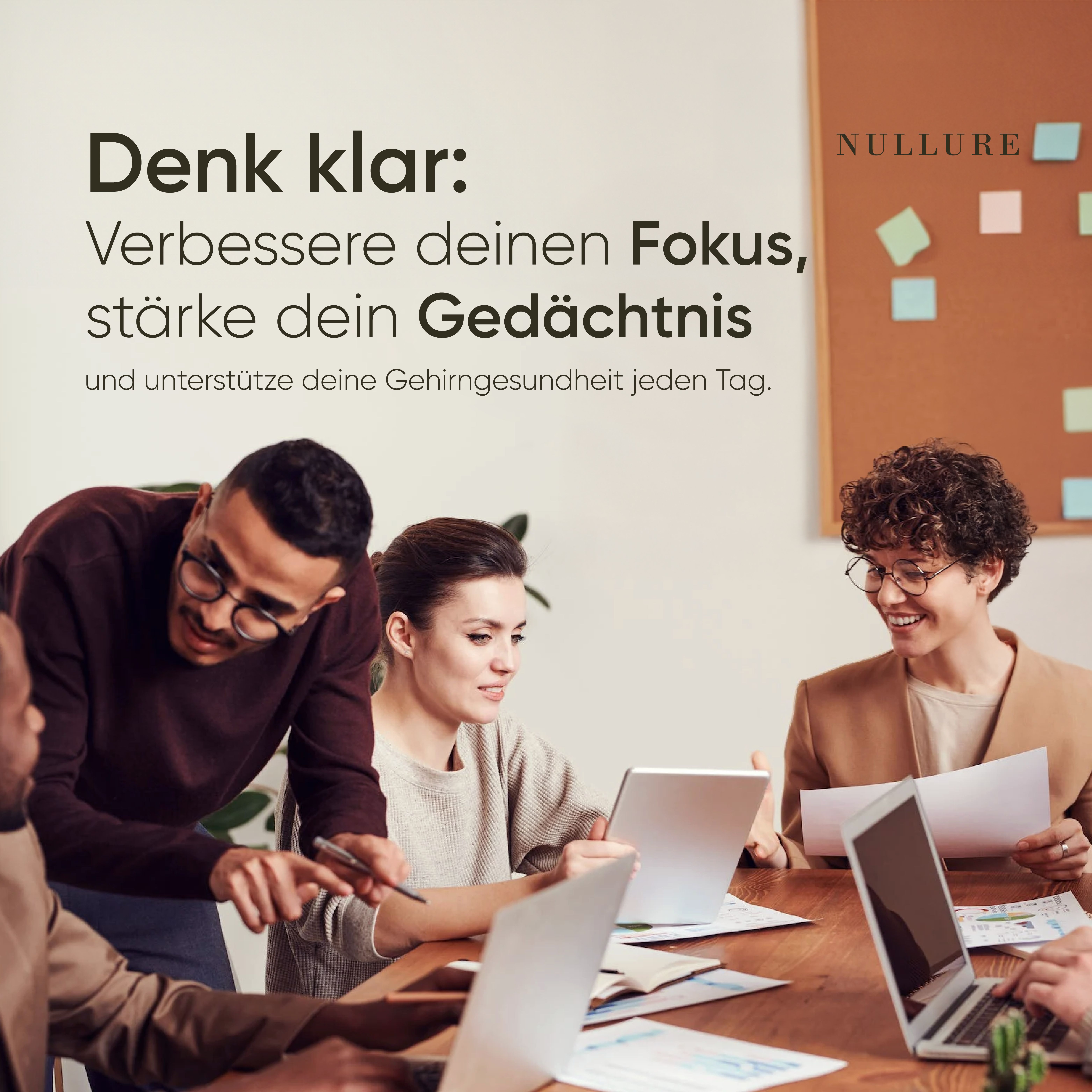 Büro mit Menschen, die an einem Tisch sitzen. Auf dem Tisch liegen Laptops und Notizen. Im Hintergrund ein Pinnwand.