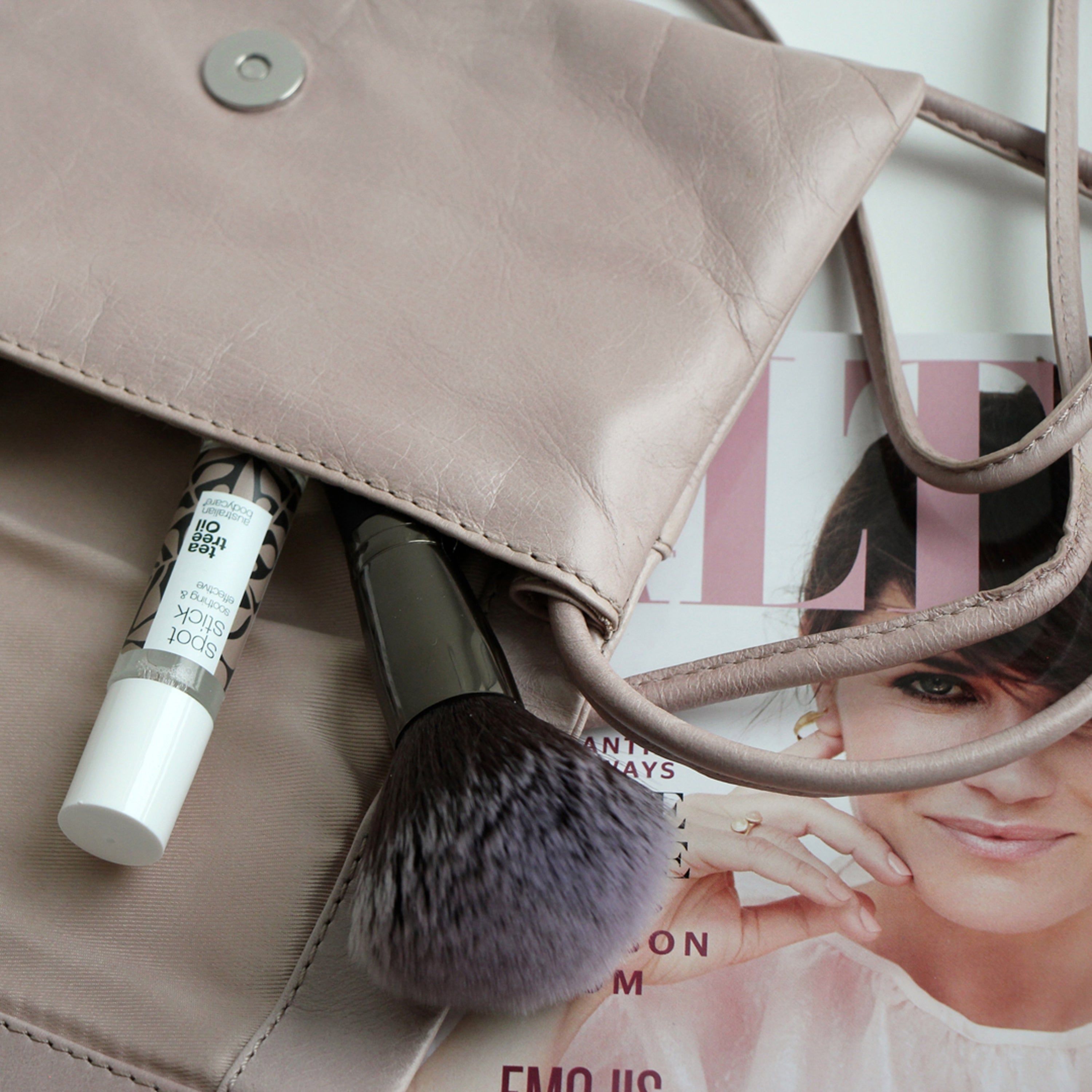 Eine Handtasche mit einem Roll-on-Stick und einem Make-up-Pinsel. Aufschrift: Spot Stick, Australian Bodycare.