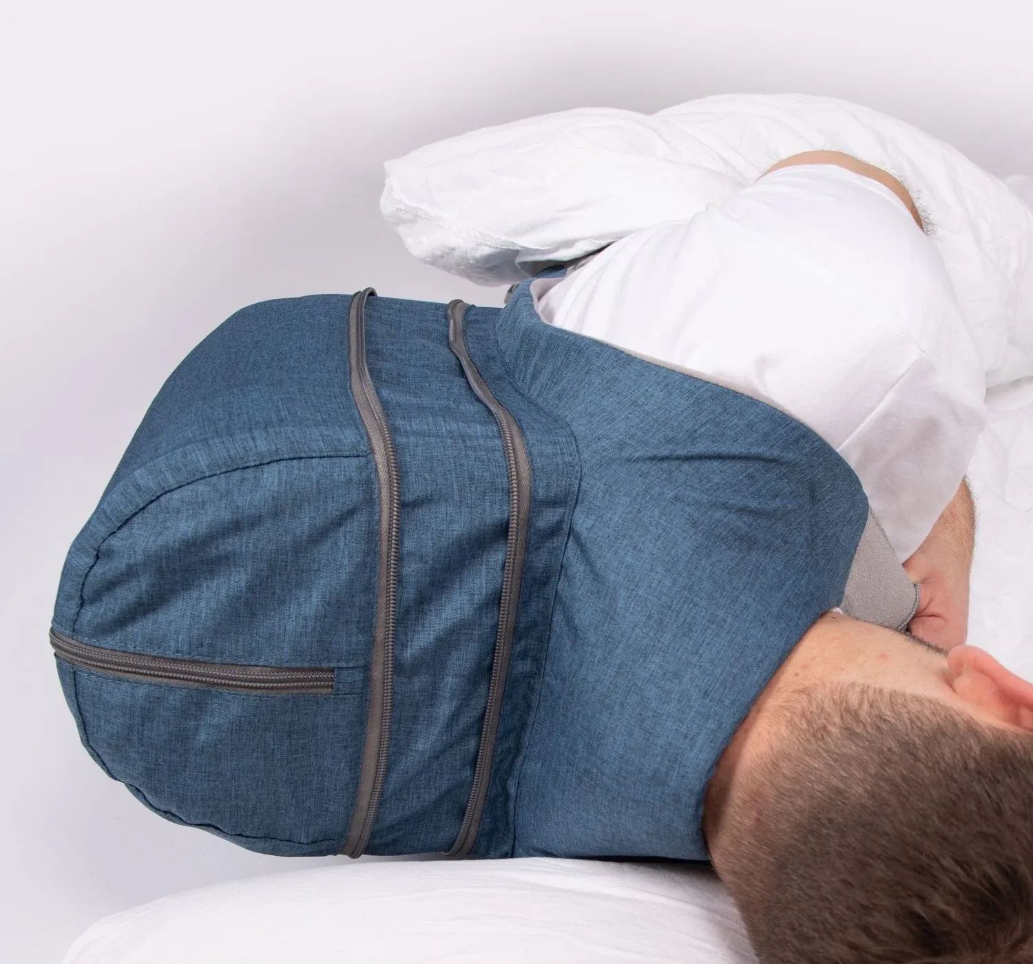 Blauer Rückenlageverhinderungsrucksack, getragen von einer Person im Bett. Graue Reißverschlüsse und Details. Person liegt auf dem Rücken.