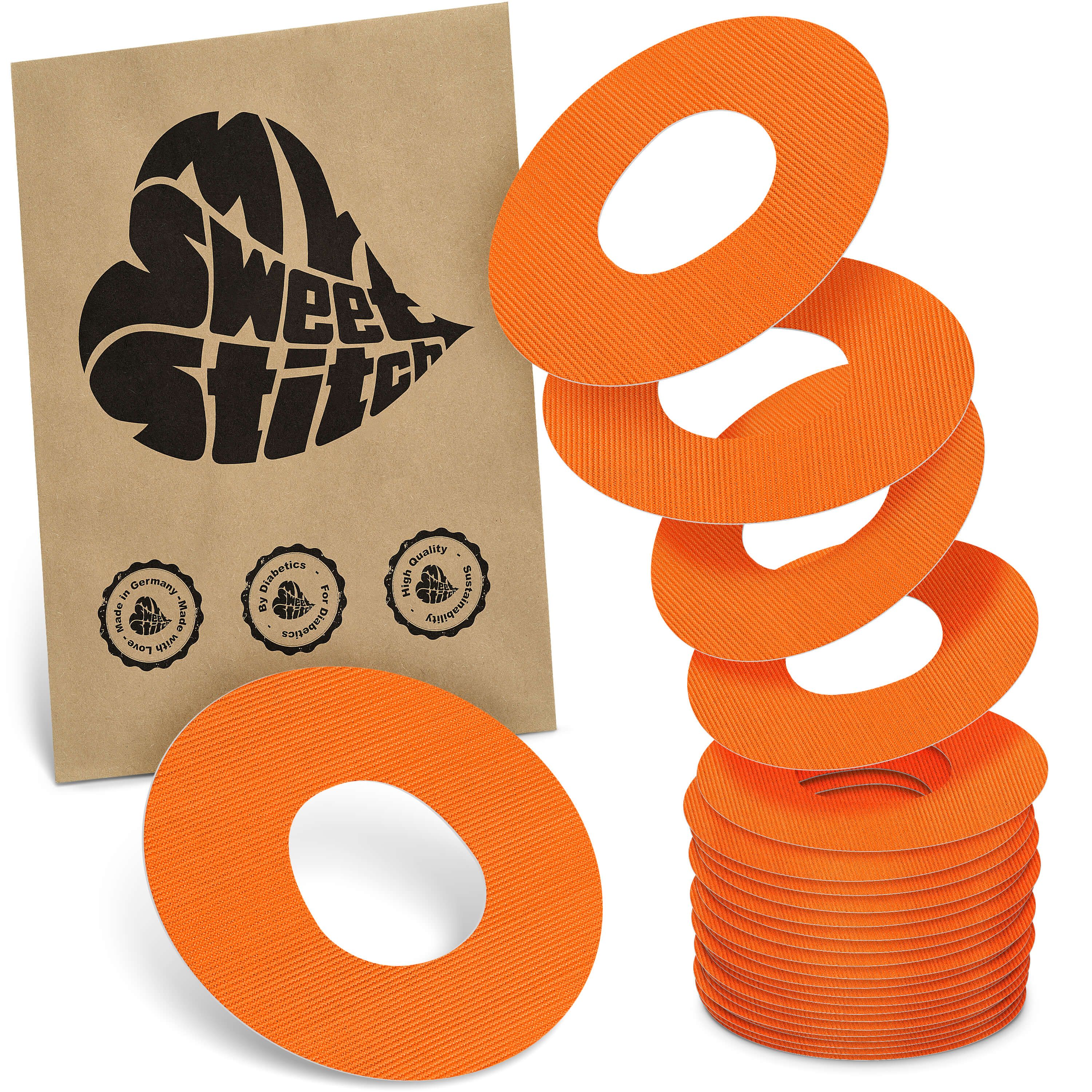 Orange, ringförmige Katheter-Pflaster mit zentraler Aussparung. Ein Stapel und ein einzelnes Pflaster sind sichtbar, daneben eine braune Verpackung mit Logo.