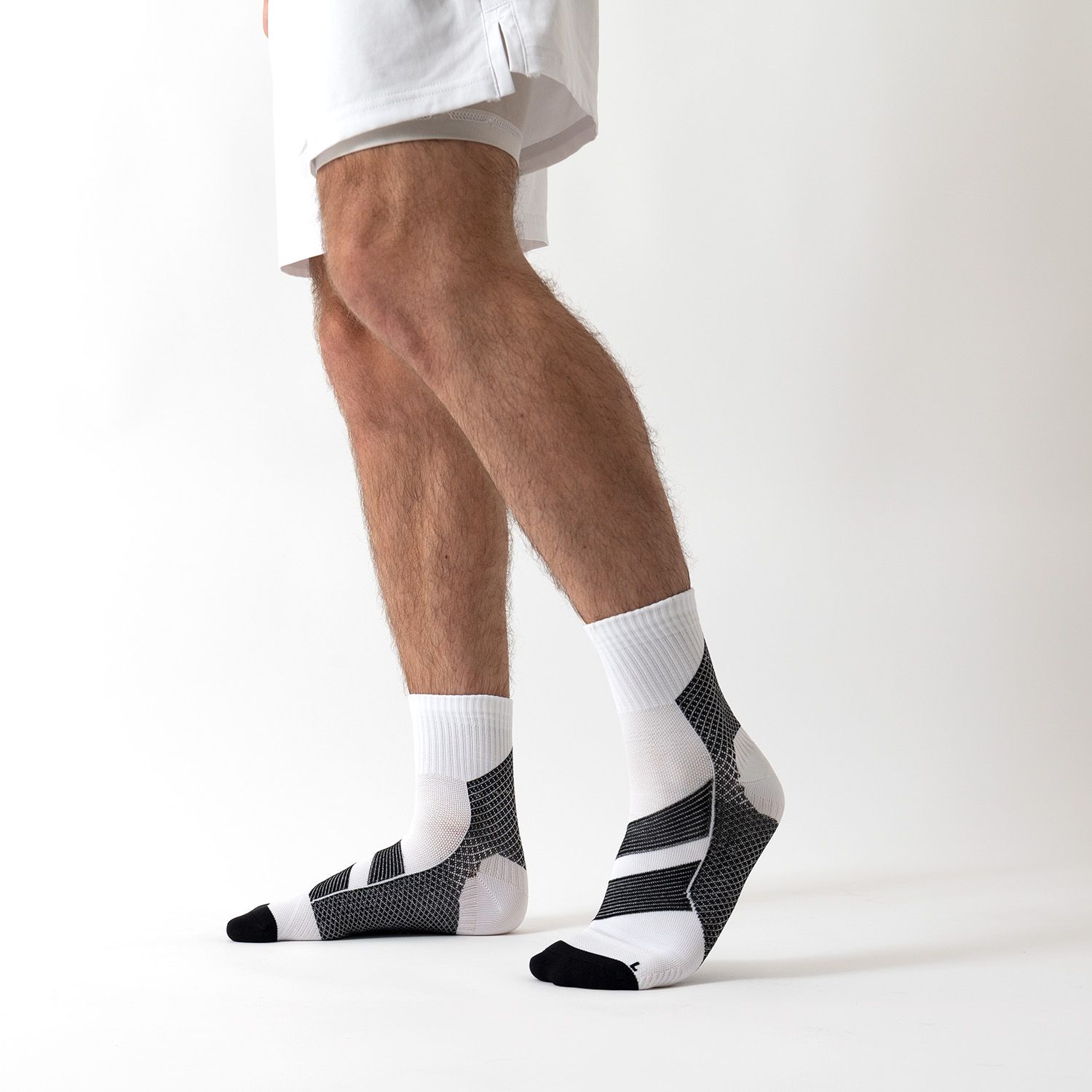 Person trägt weiße und schwarze Kompressionssocken. Der Knöchelbereich ist weiß, mit schwarzen Details und Streifen. Der Fuß ist schwarz.