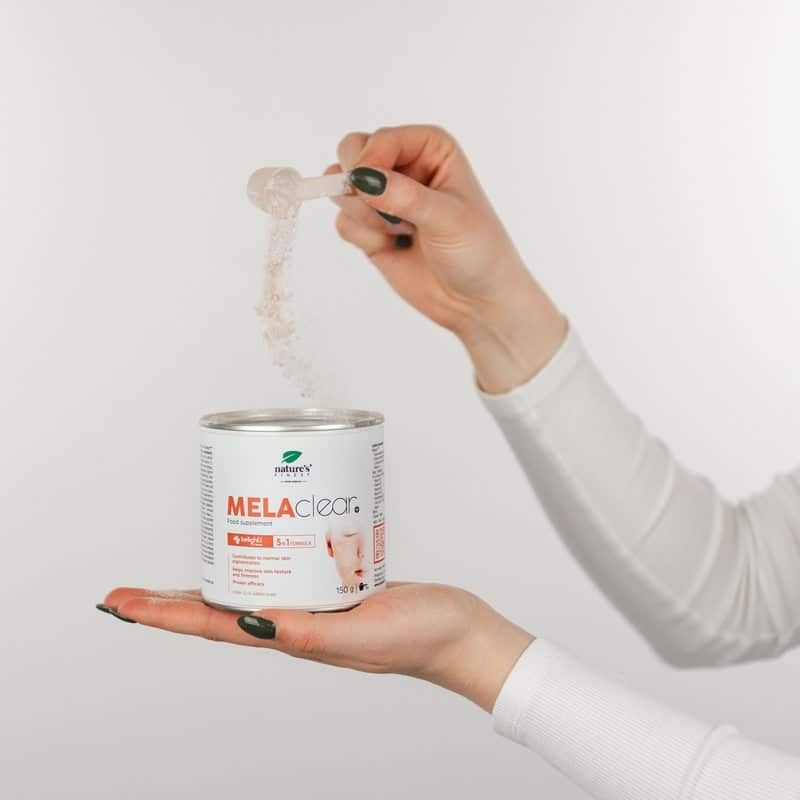 Hand gibt Pulver aus Löffel in Dose MELAclear+. Produkt für ebenmäßigen Hautton.