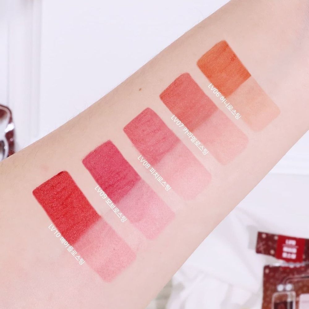 Arm mit fünf Lippenfarben-Swatches. Farben von hellrosa bis orange. Text: 'LV06 Honey Roasting' etc.