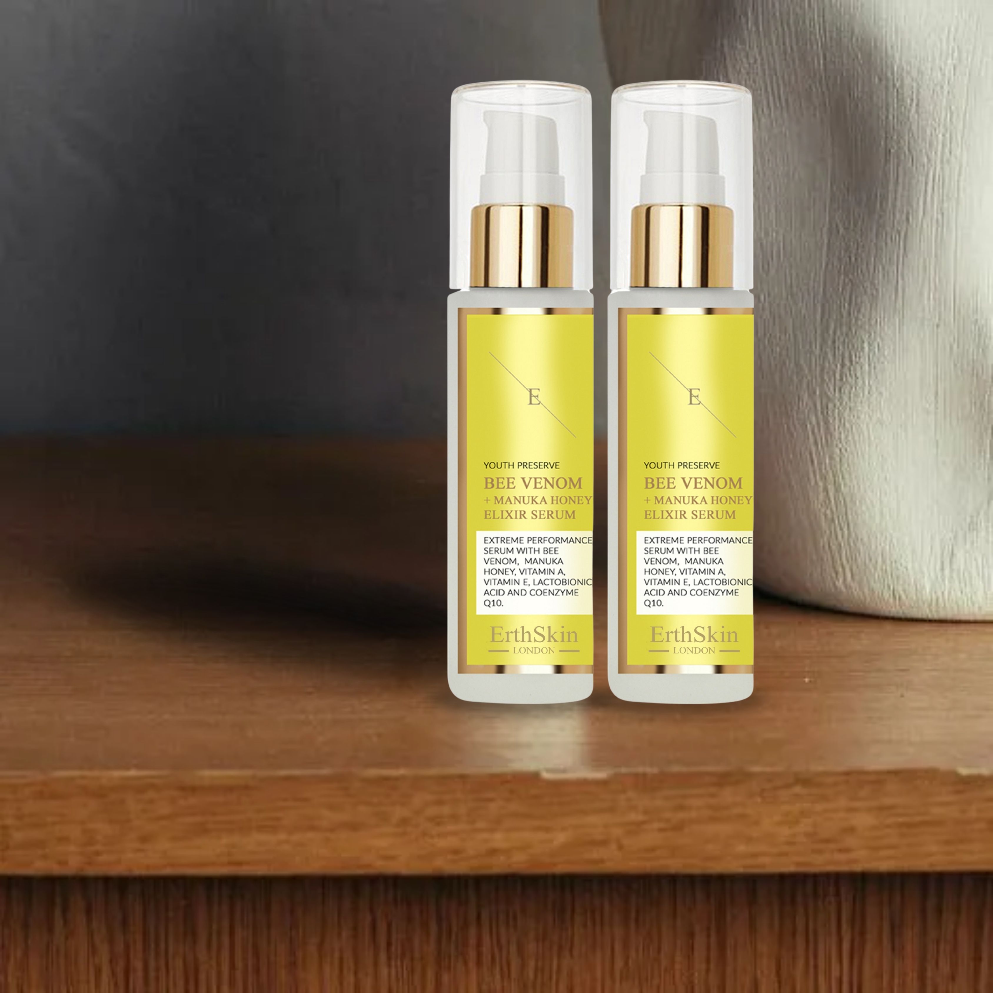 Zwei Serumflaschen mit gelben Etiketten, goldfarbenen Pumpköpfen und transparenten Kappen. Text: "ErthSkin London" und "Bee Venom + Manuka Honey Elixir Serum".