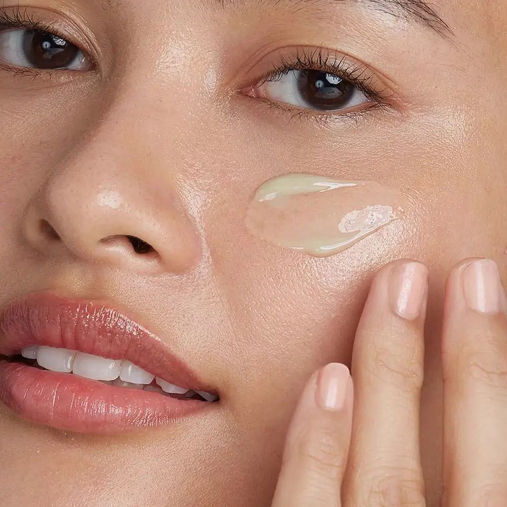 Gesicht einer Person mit aufgetragener Creme. Creme ist hellgrün und wird mit dem Finger aufgetragen.