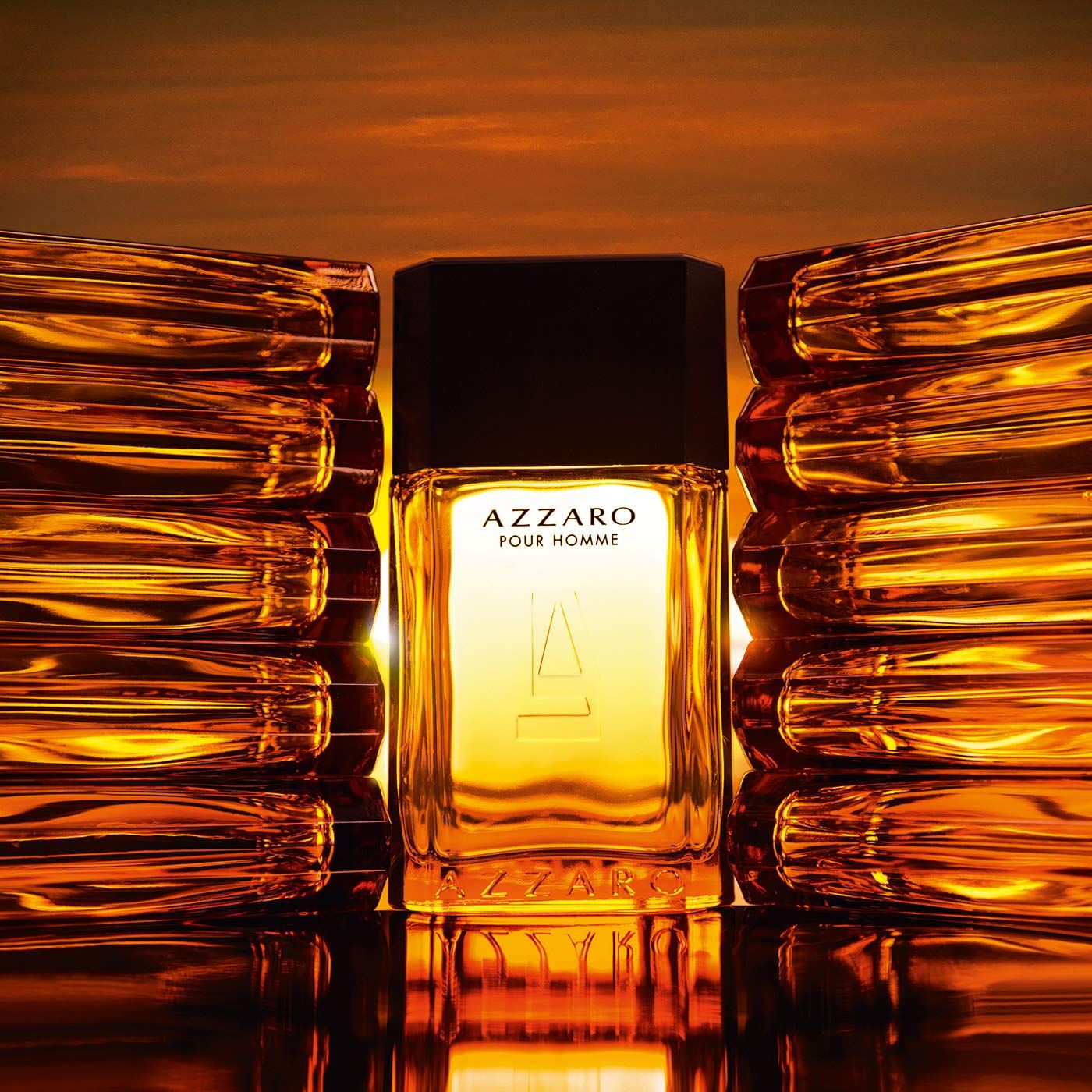 Azzaro Pour Homme Flakon. Rechteckiger Flakon mit schwarzem Deckel. Gelbe Flüssigkeit. Umgeben von goldenen Elementen.