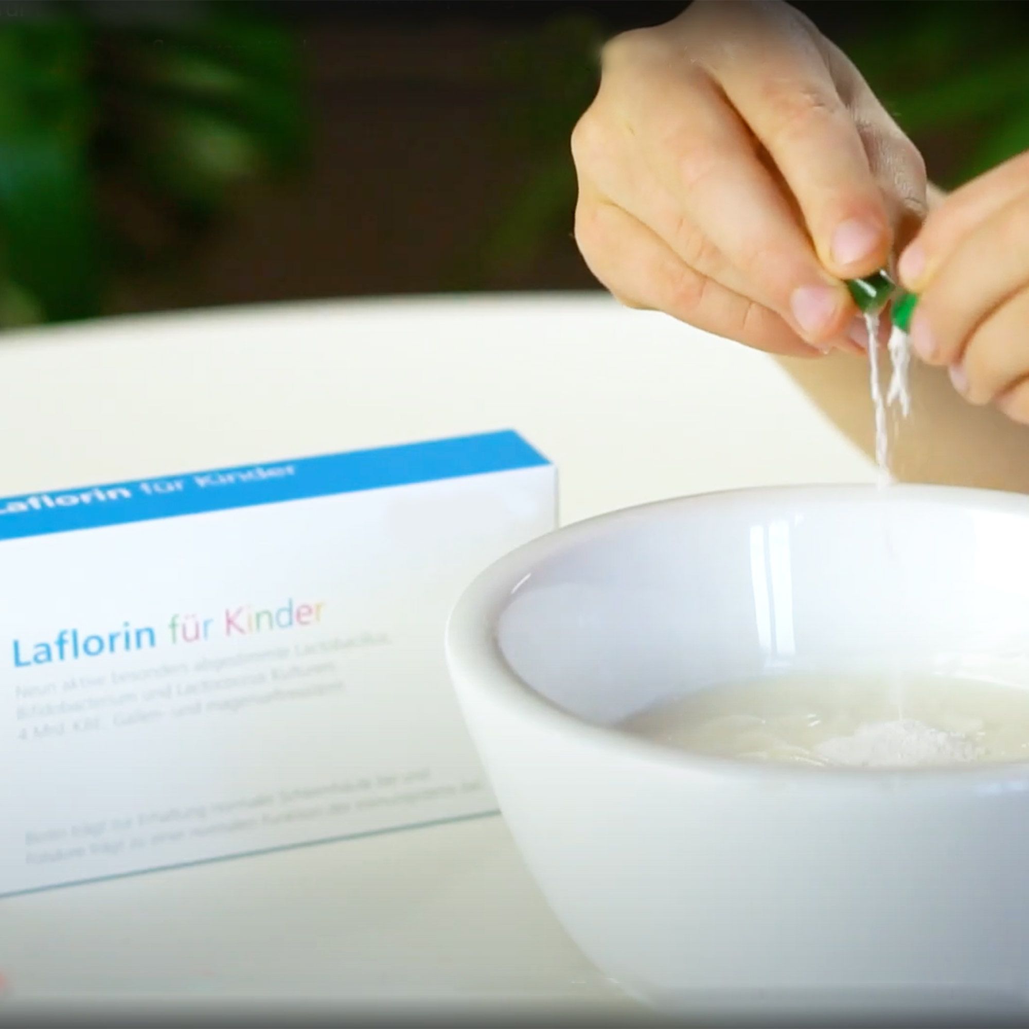 Kind öffnet Kapsel über einer Schüssel. Laflorin für Kinder-Verpackung im Hintergrund. Weißer Inhalt wird freigesetzt.