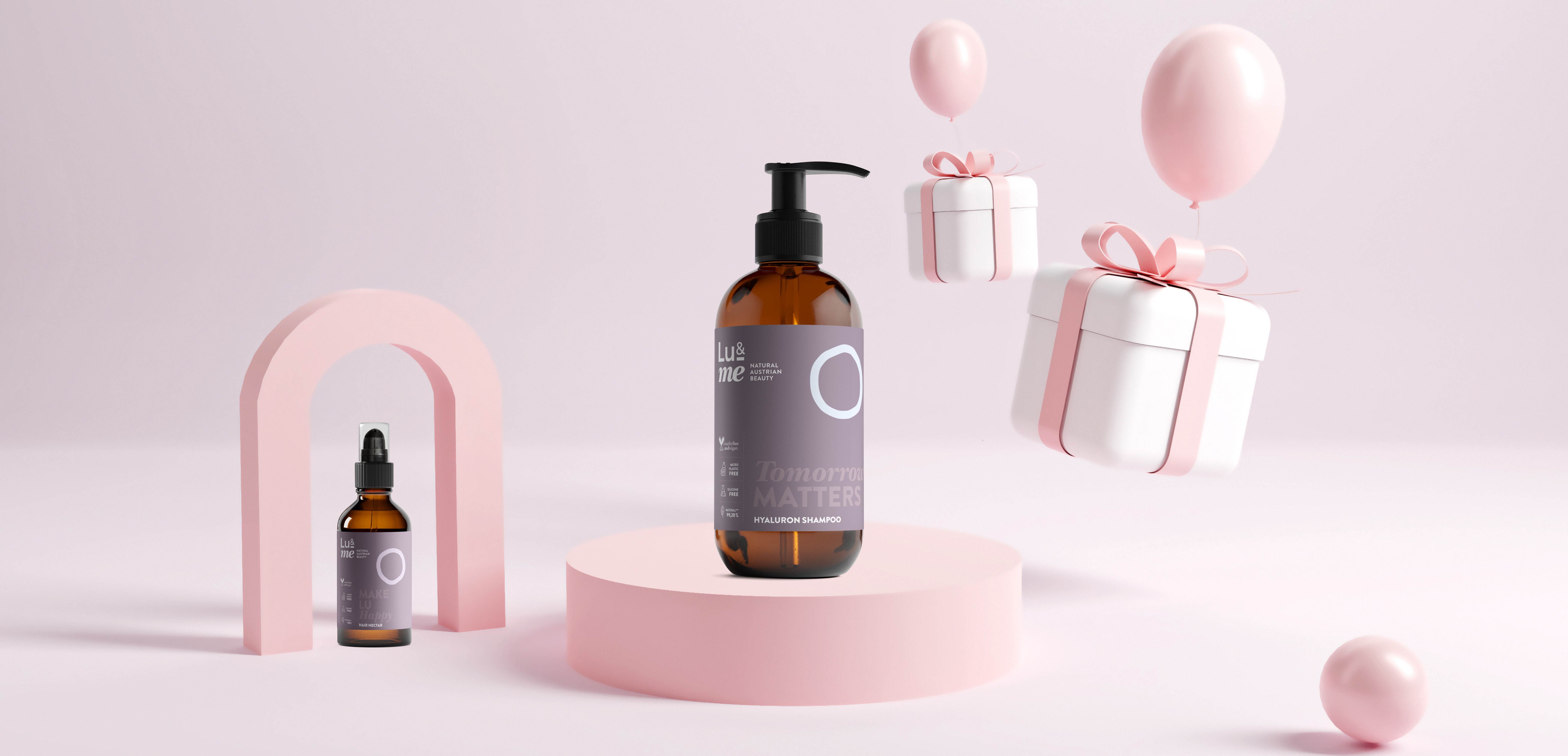 Braune Flaschen mit Pump- und Pipettenaufsatz. Aufschrift: Lu&me. Auf rosa Podest. Geschenkboxen und Ballons im Hintergrund.