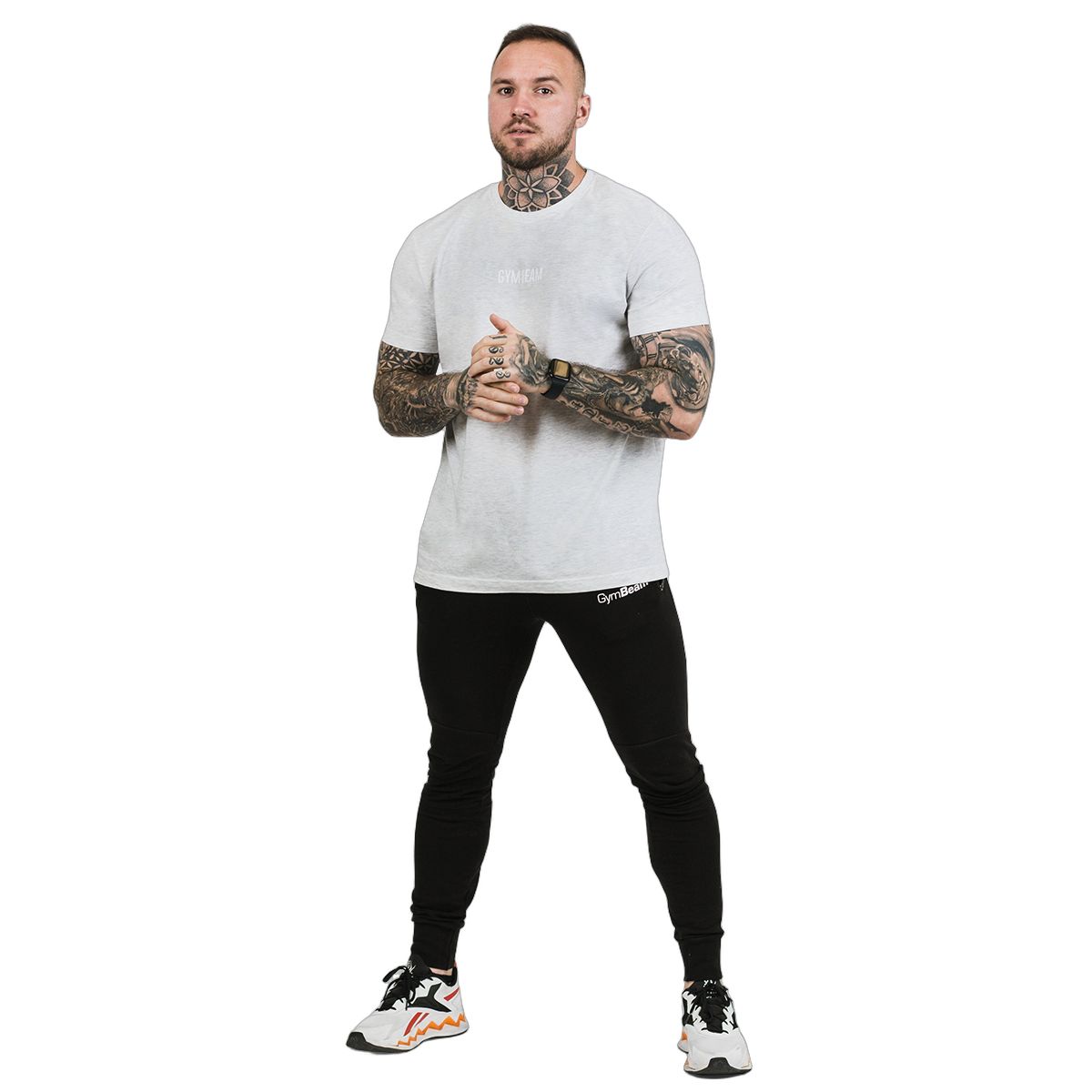 Ein Mann in einem grauen GymBeam T-Shirt und schwarzen Hosen, stehend.