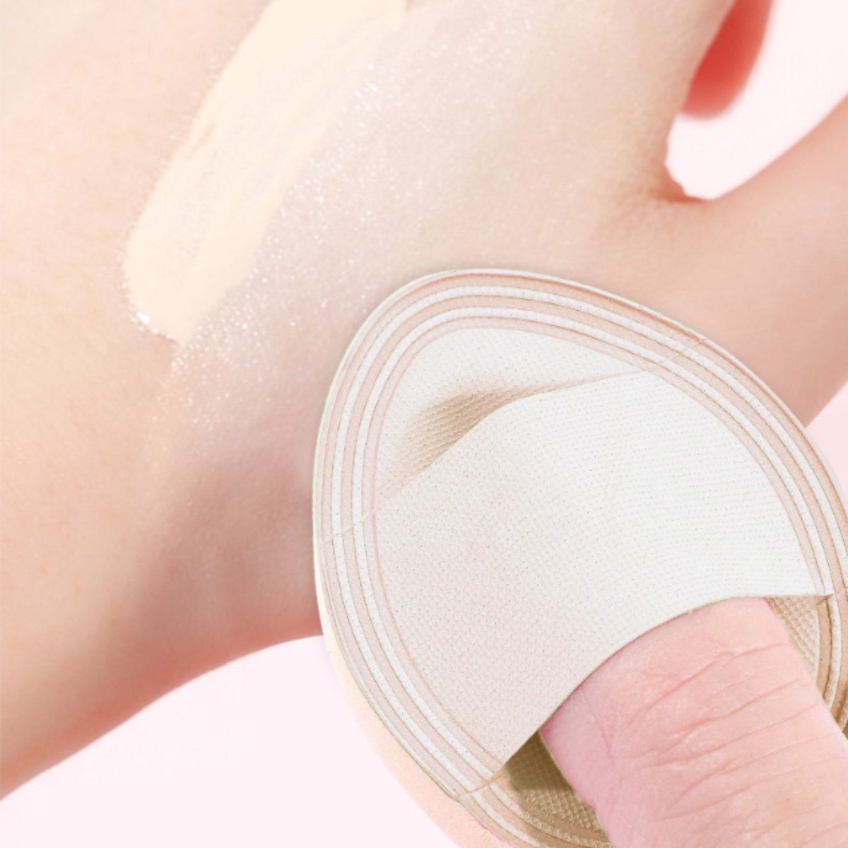 Ein beiger Make-up-Schwamm mit einem Finger darin, der auf einer Handfläche aufgetragen wird.